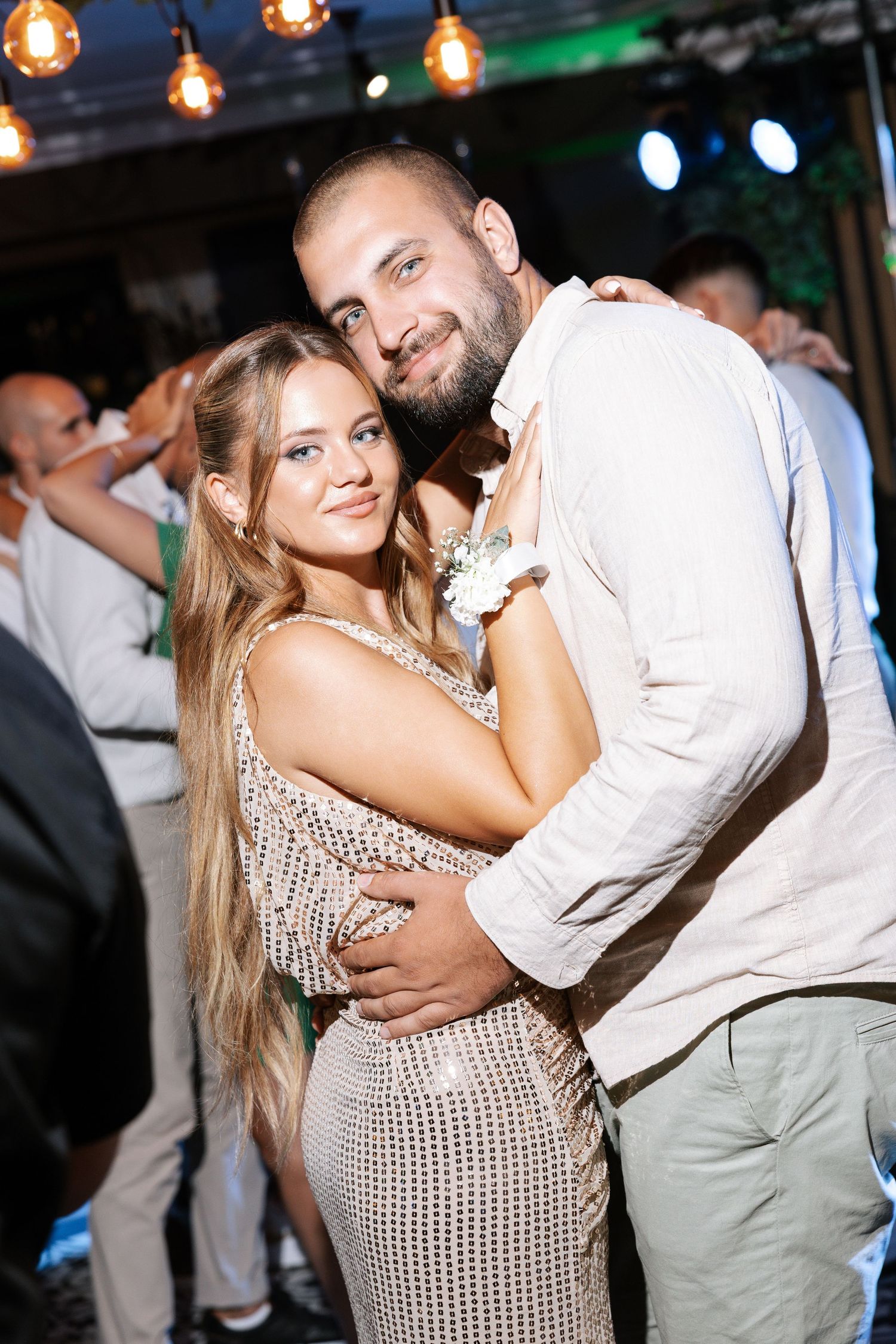 A couple shares an intimate dance together at an evening event with string lights overhead.