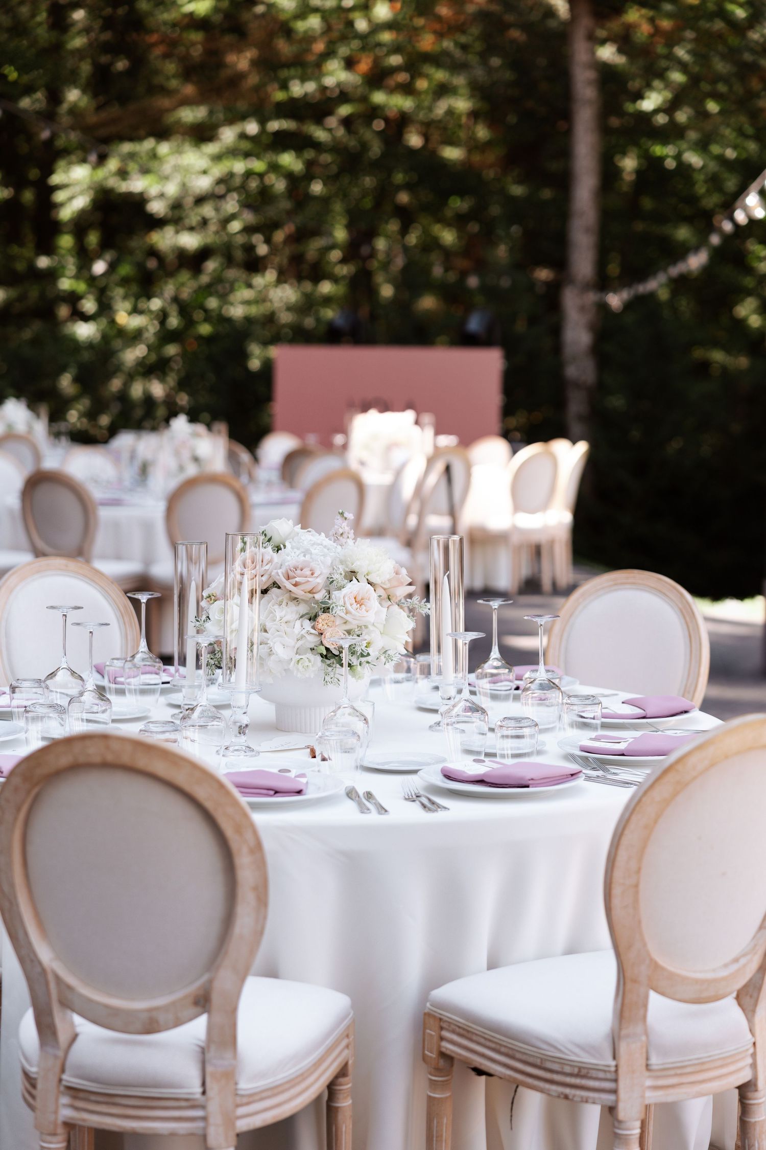 Elegant wedding reception table setting with white linens and French-style chairs.