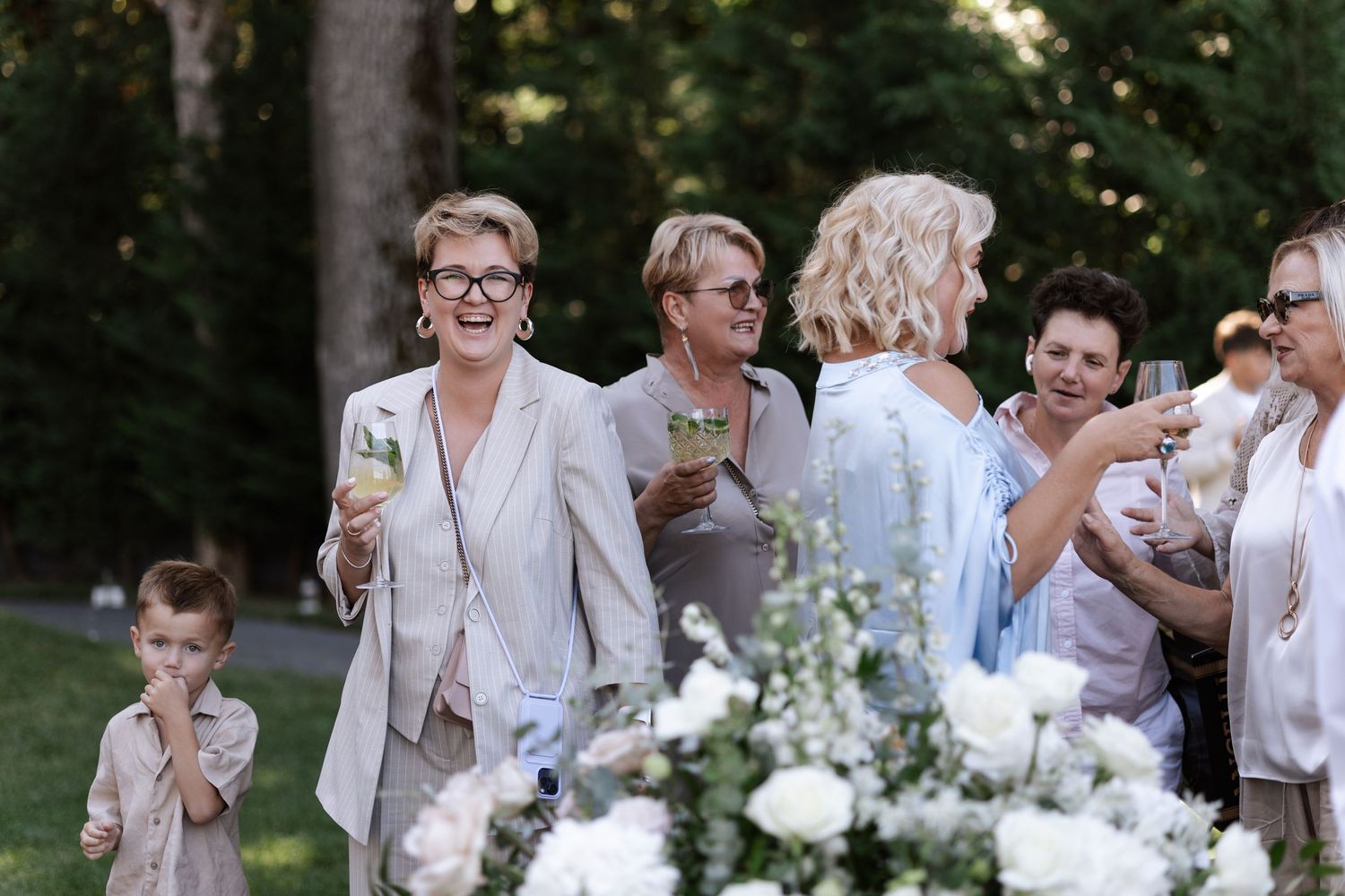 Wedding party celebrates outdoors with white floral arrangements and light colored attire.