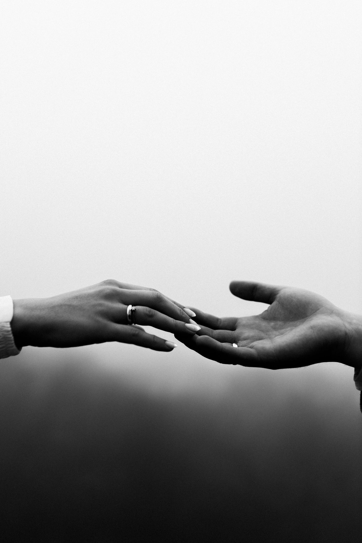 A minimalist black and white photo of two hands reaching towards each other with wedding rings.