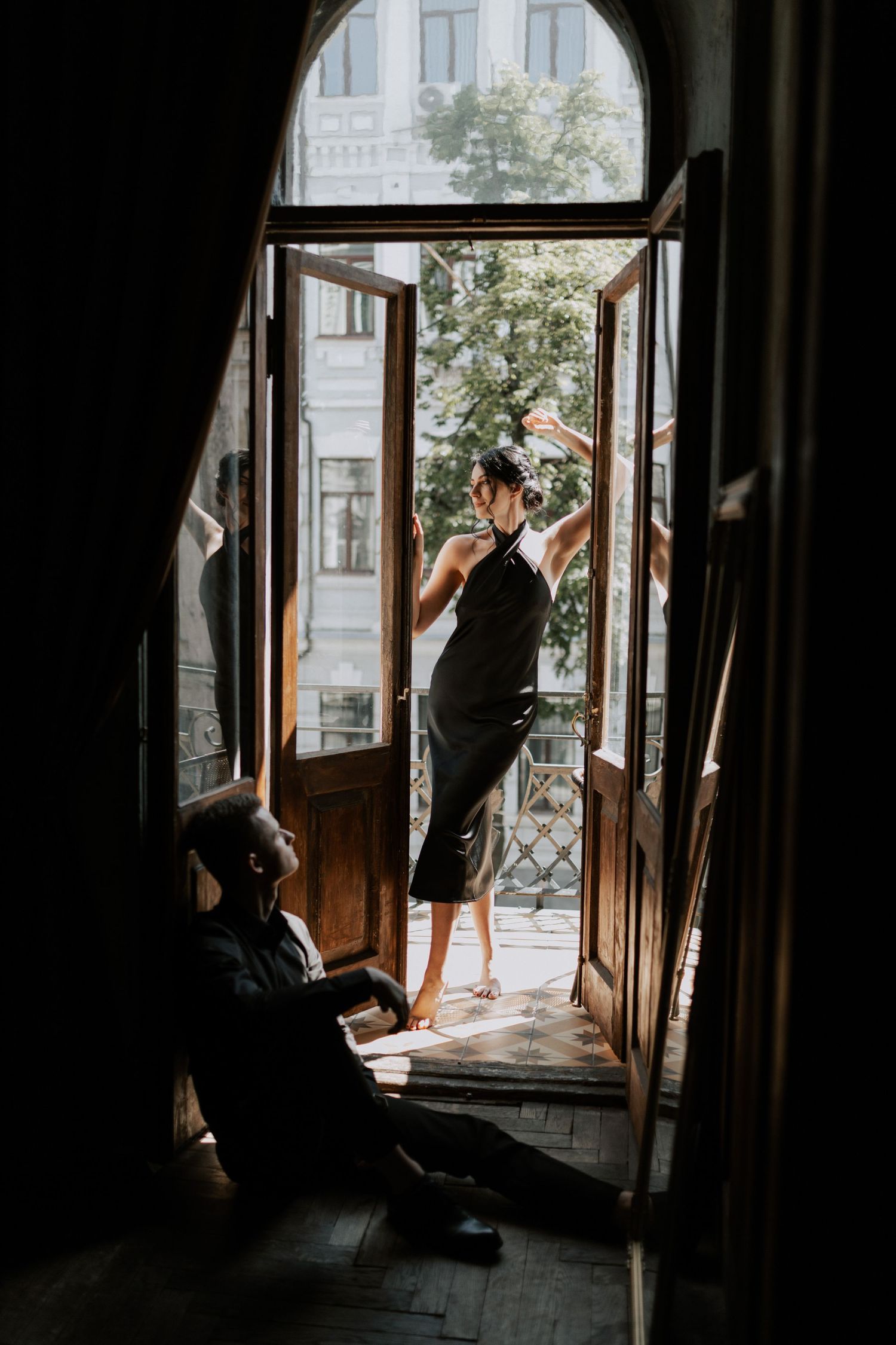 Two figures in silhouette by an open arched window in a vintage apartment.