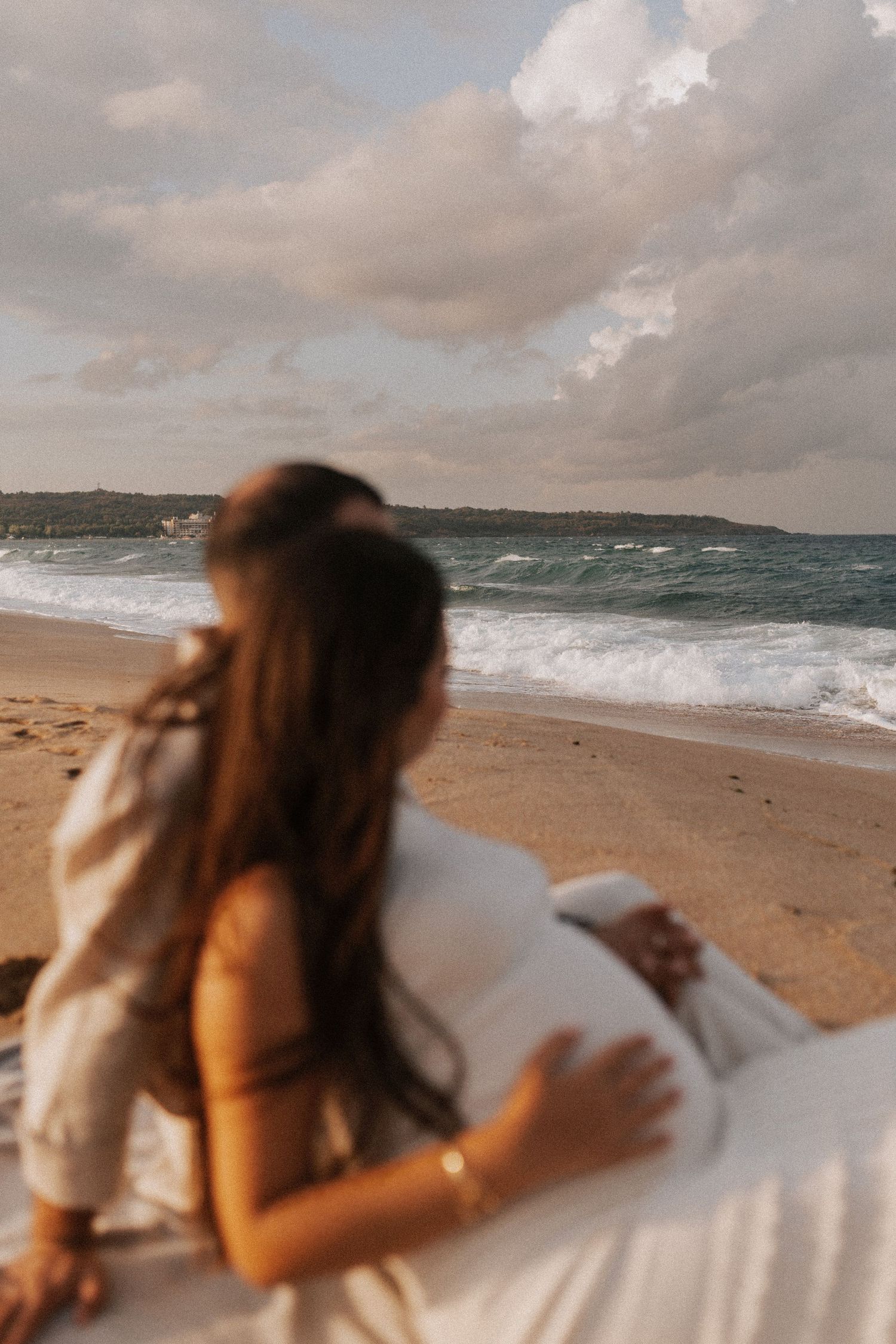 A person in white relaxing on a sandy beach at sunset with waves crashing in the background.
