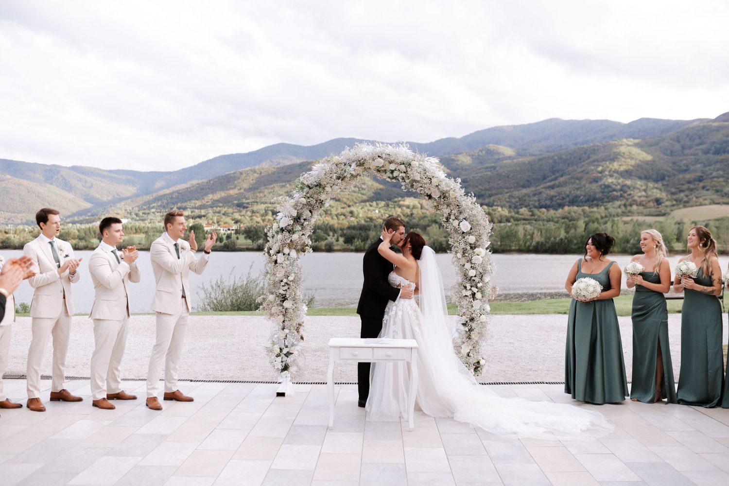 Wedding ceremony with bridal party in white and sage green against mountain backdrop.