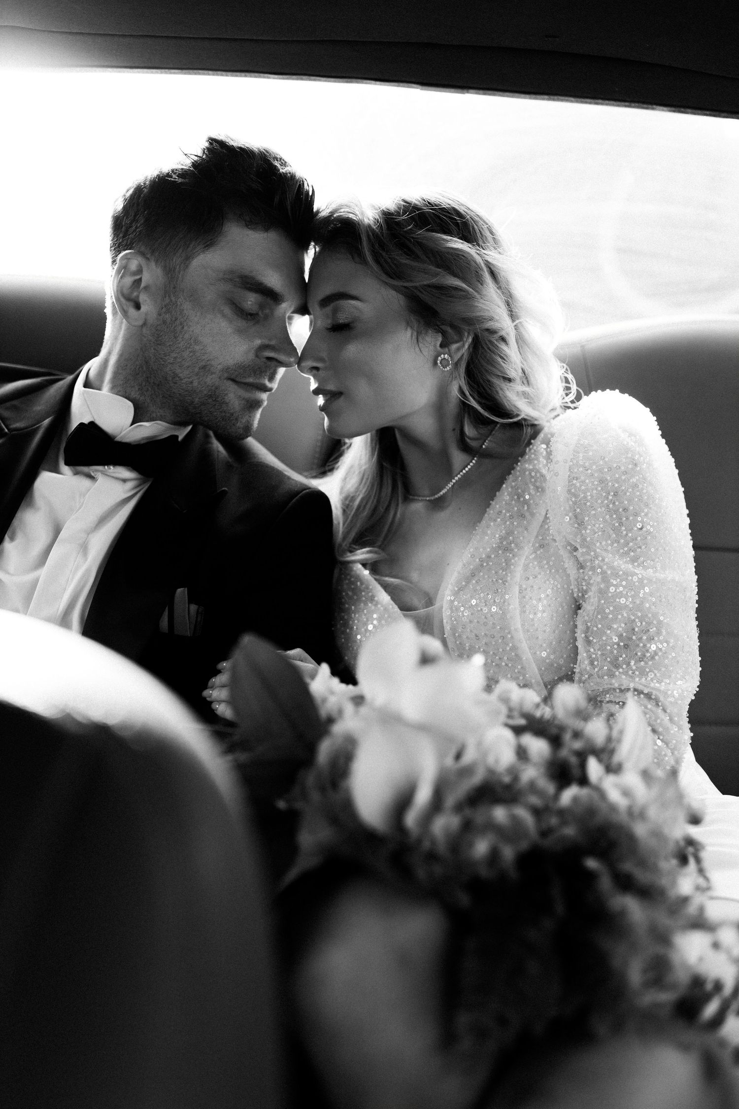 Intimate black and white portrait of wedding couple sharing tender moment in car.