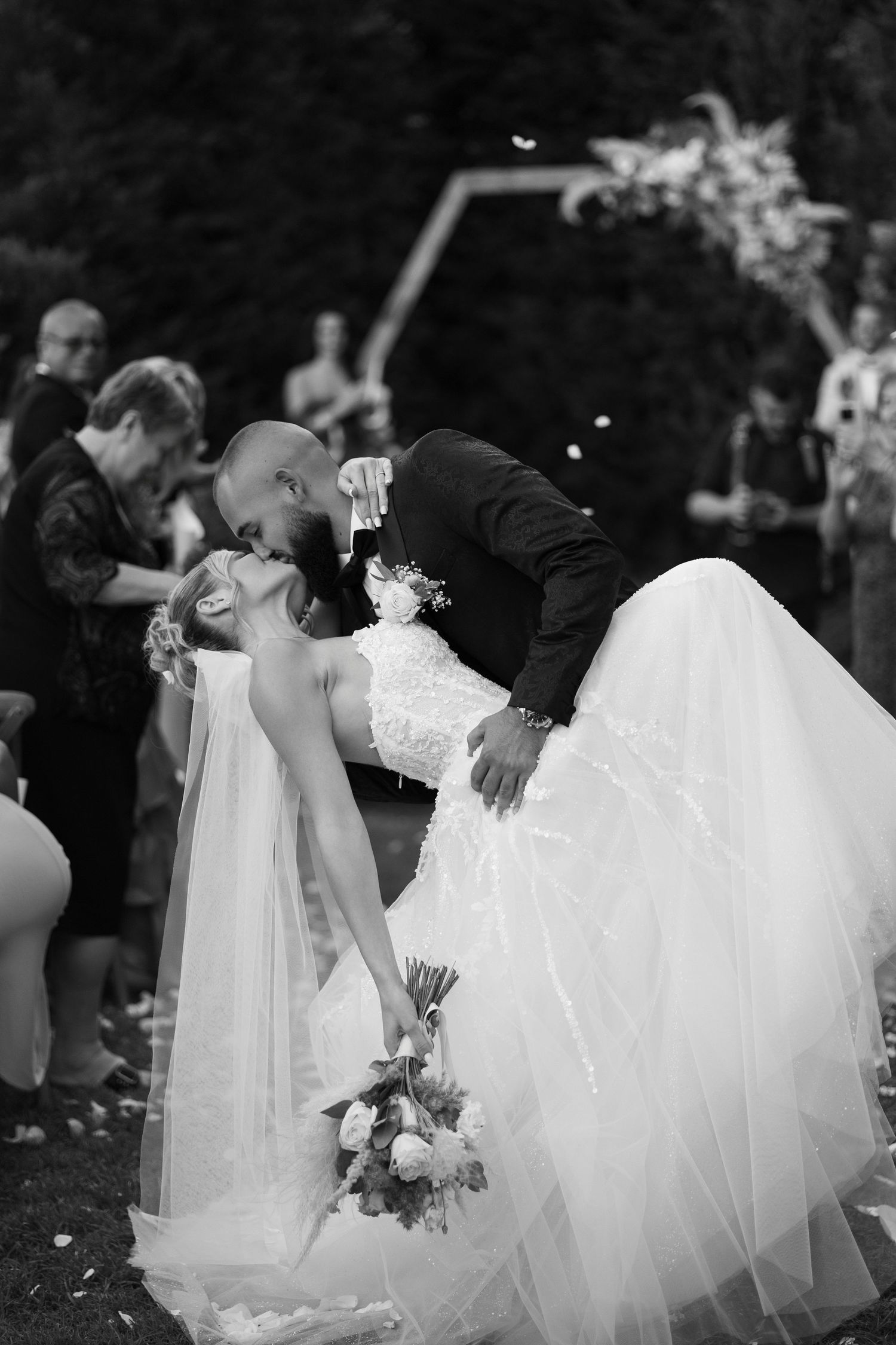 A romantic black and white wedding photo showing a dramatic dip kiss between newlyweds while the bride holds her bouquet.