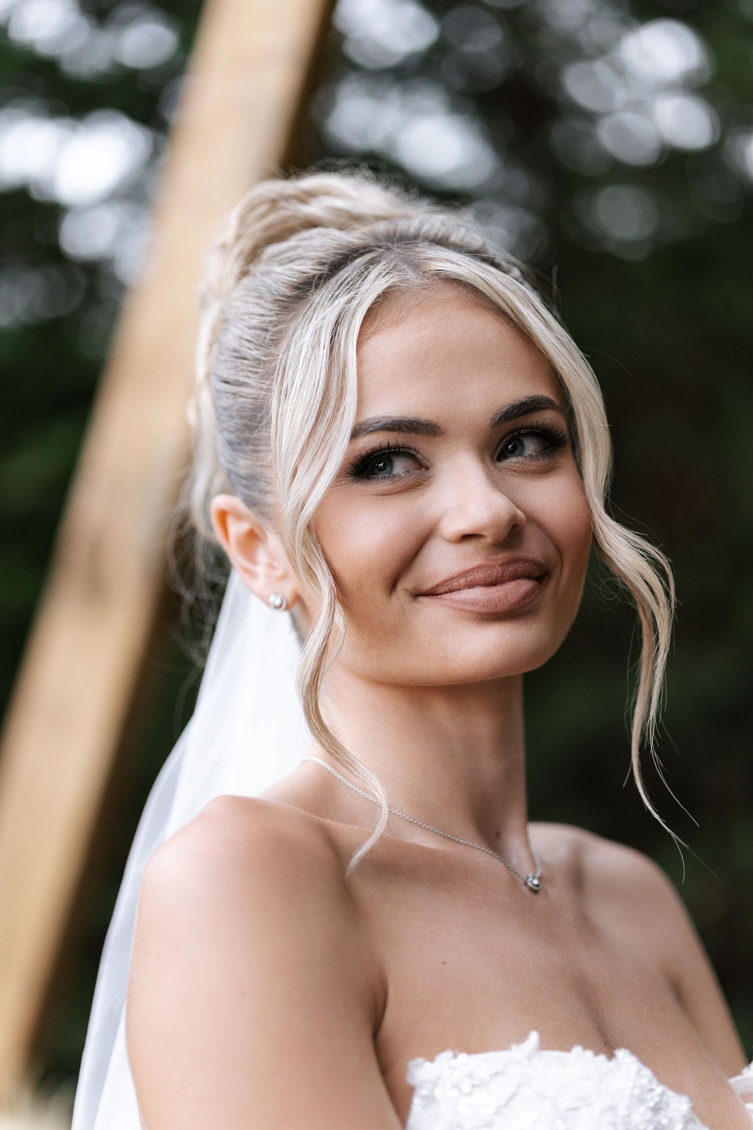 Elegant portrait of someone in a white dress against a soft natural outdoor background with bokeh effect.