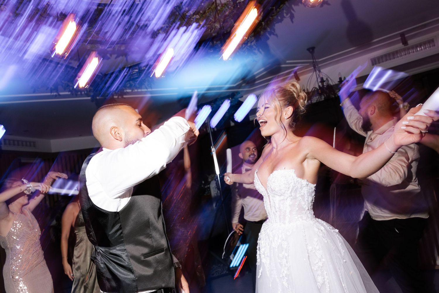 Wedding party dancing energetically on the dance floor with colorful lights and motion blur effects in the background.