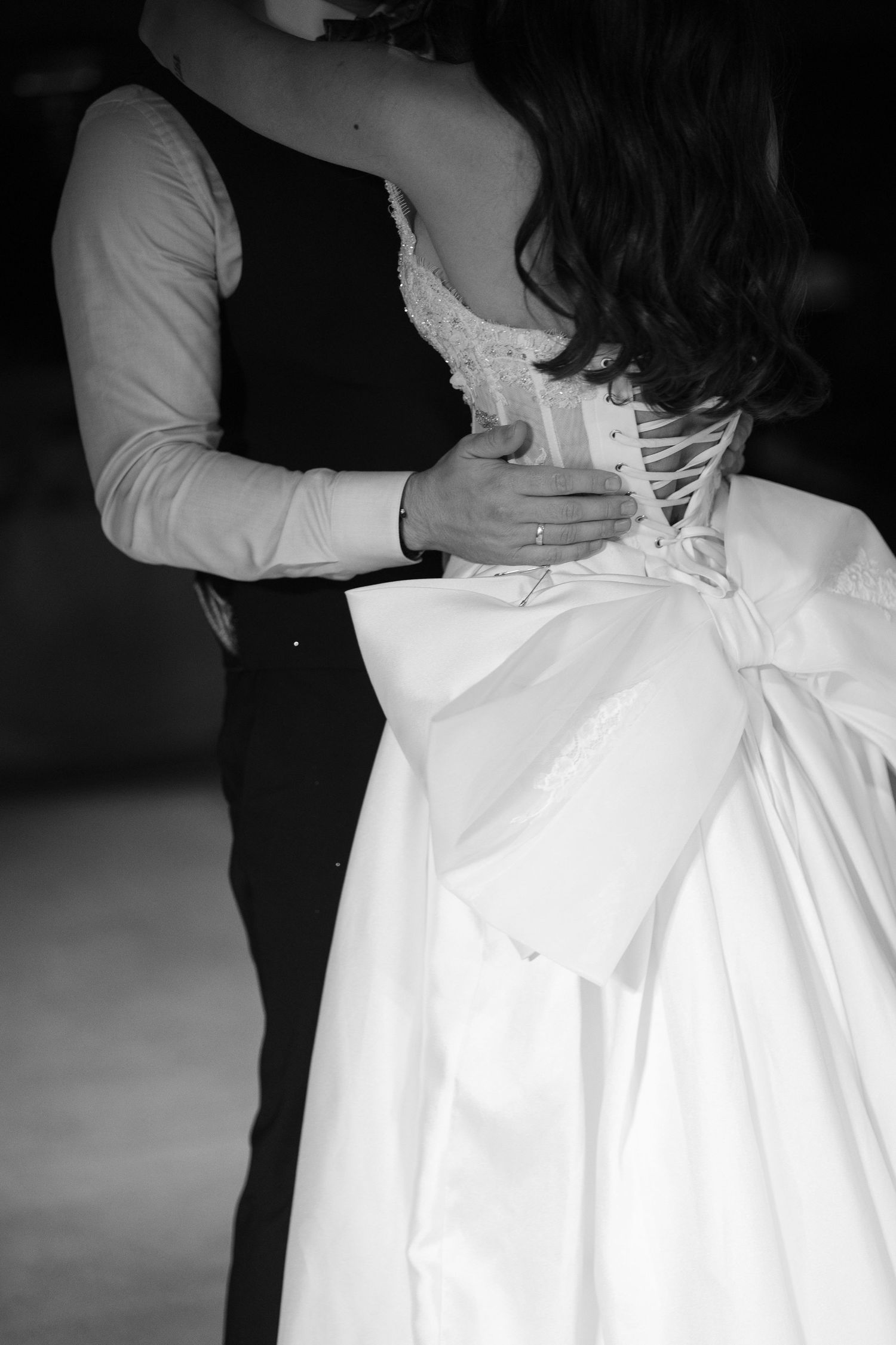 Black and white series showing the back details of a white wedding dress being laced up in a corset style.