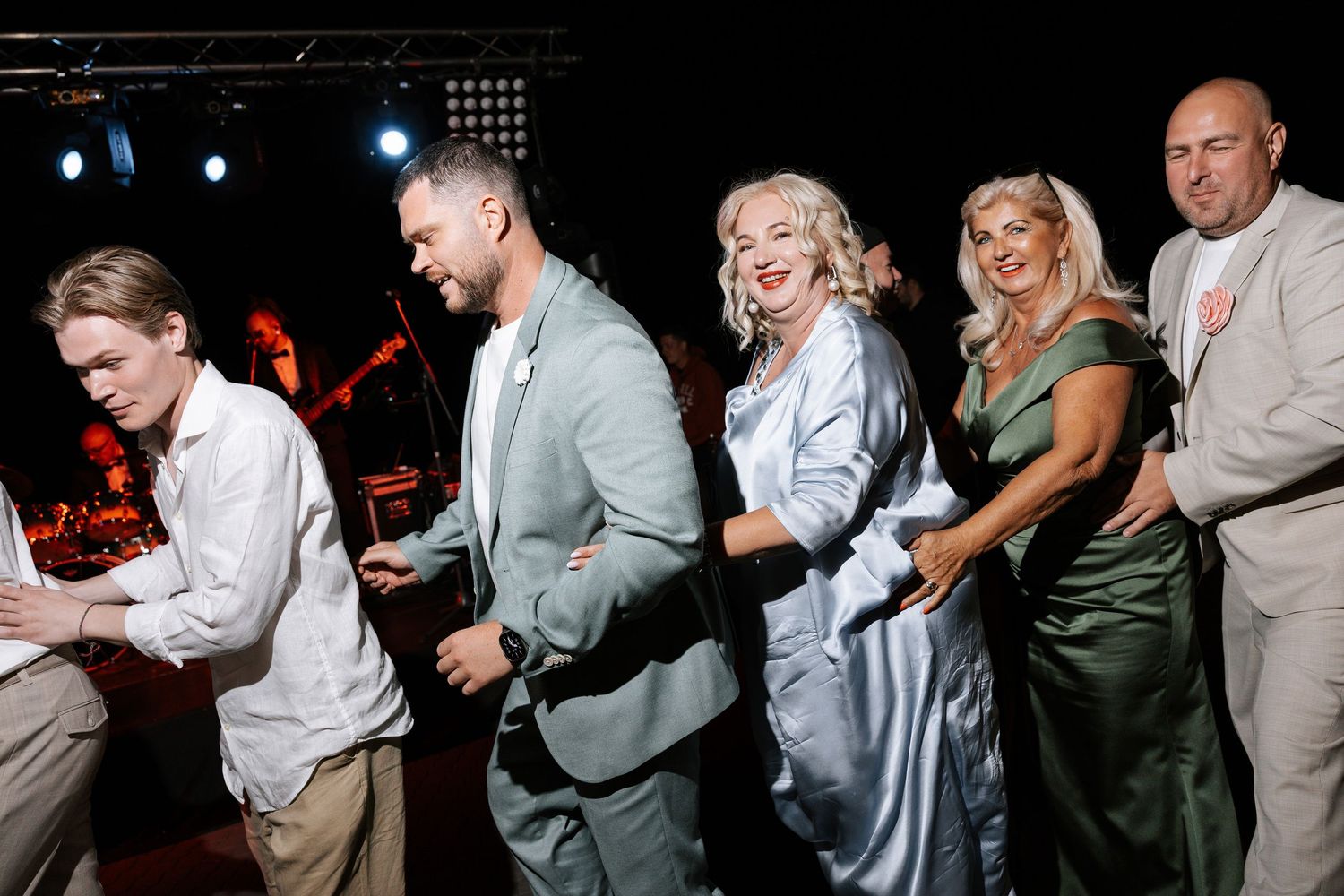 Wedding guests dance and celebrate on a dimly lit dance floor.