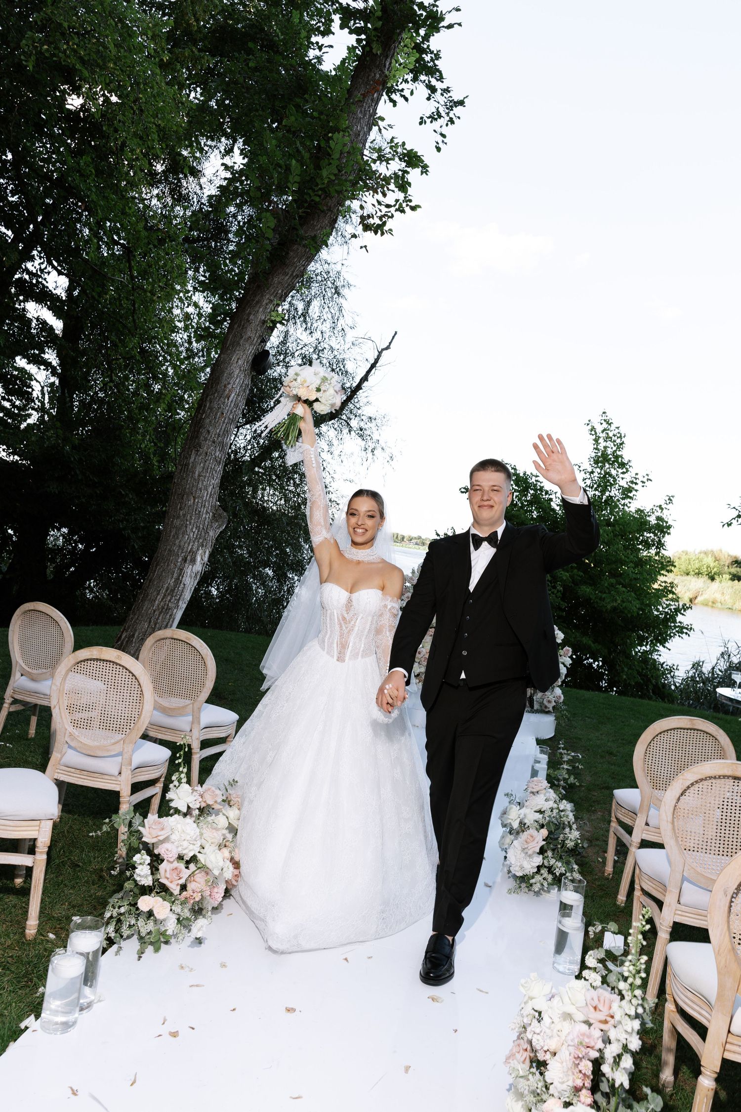 Newlyweds walking down white aisle runner at outdoor garden wedding ceremony.