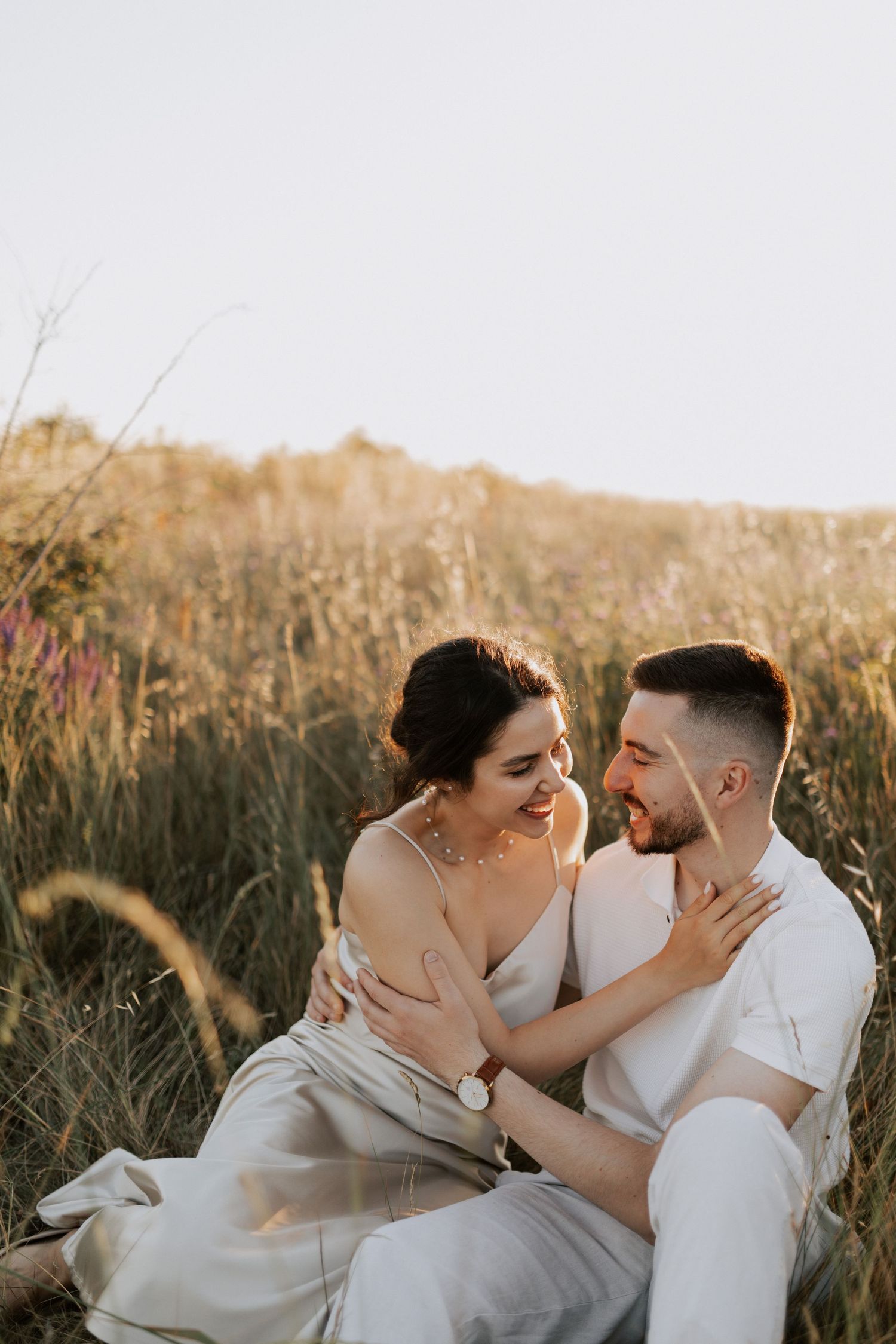 Romantic couple sharing tender moments in tall grass during golden hour.