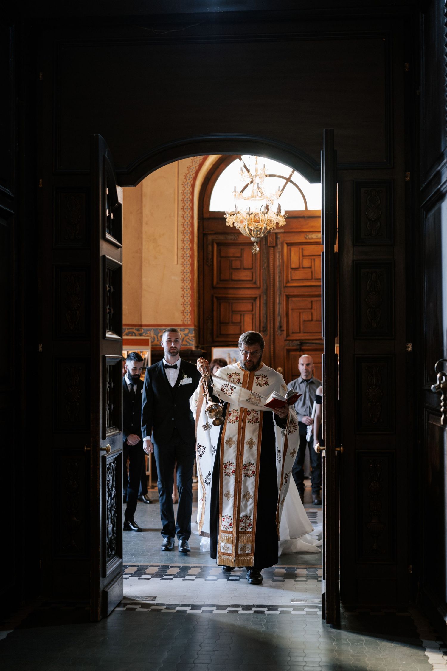 Orthodox priest leads wedding ceremony through grand church doorway.