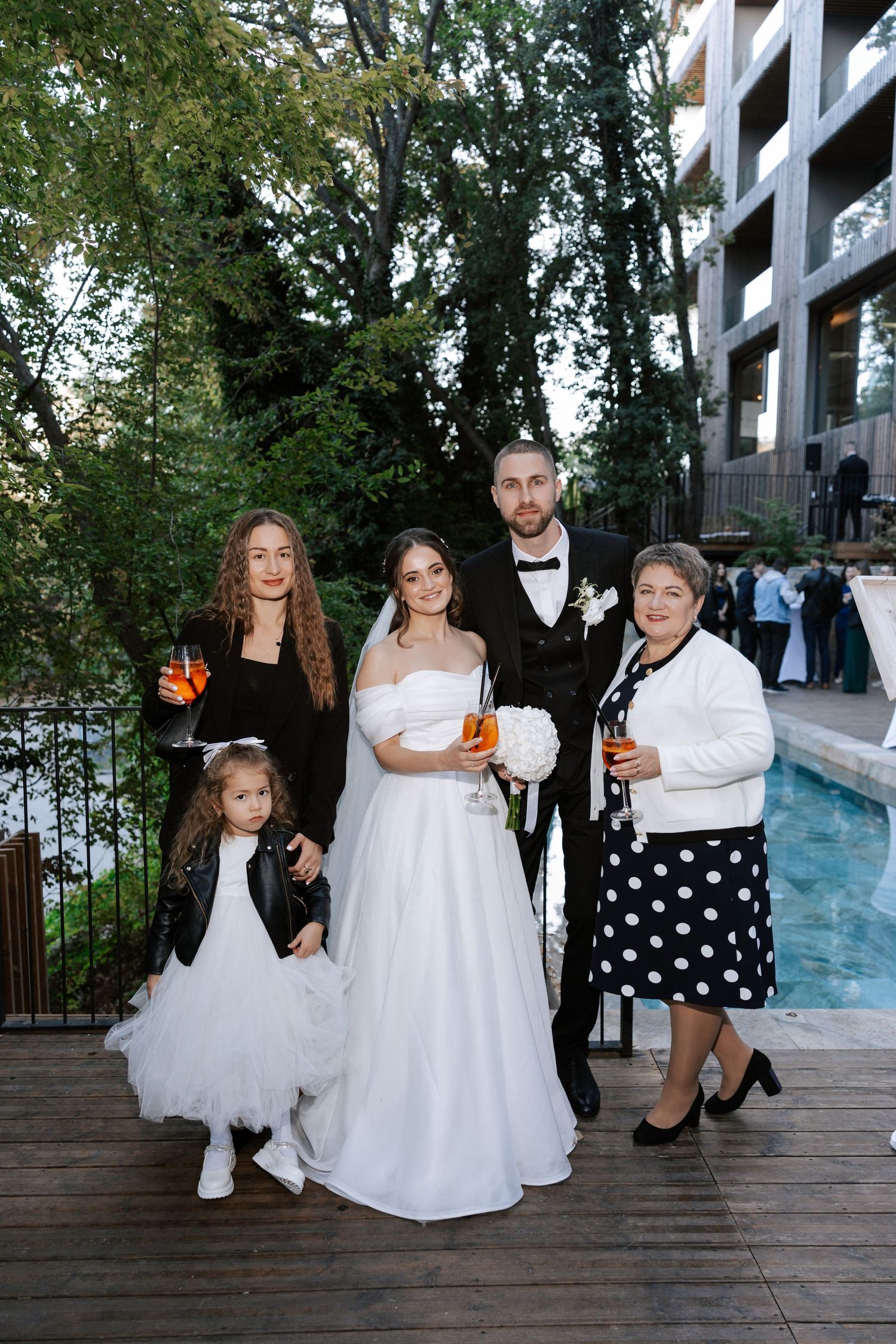 Wedding group photo on poolside deck with modern building backdrop.