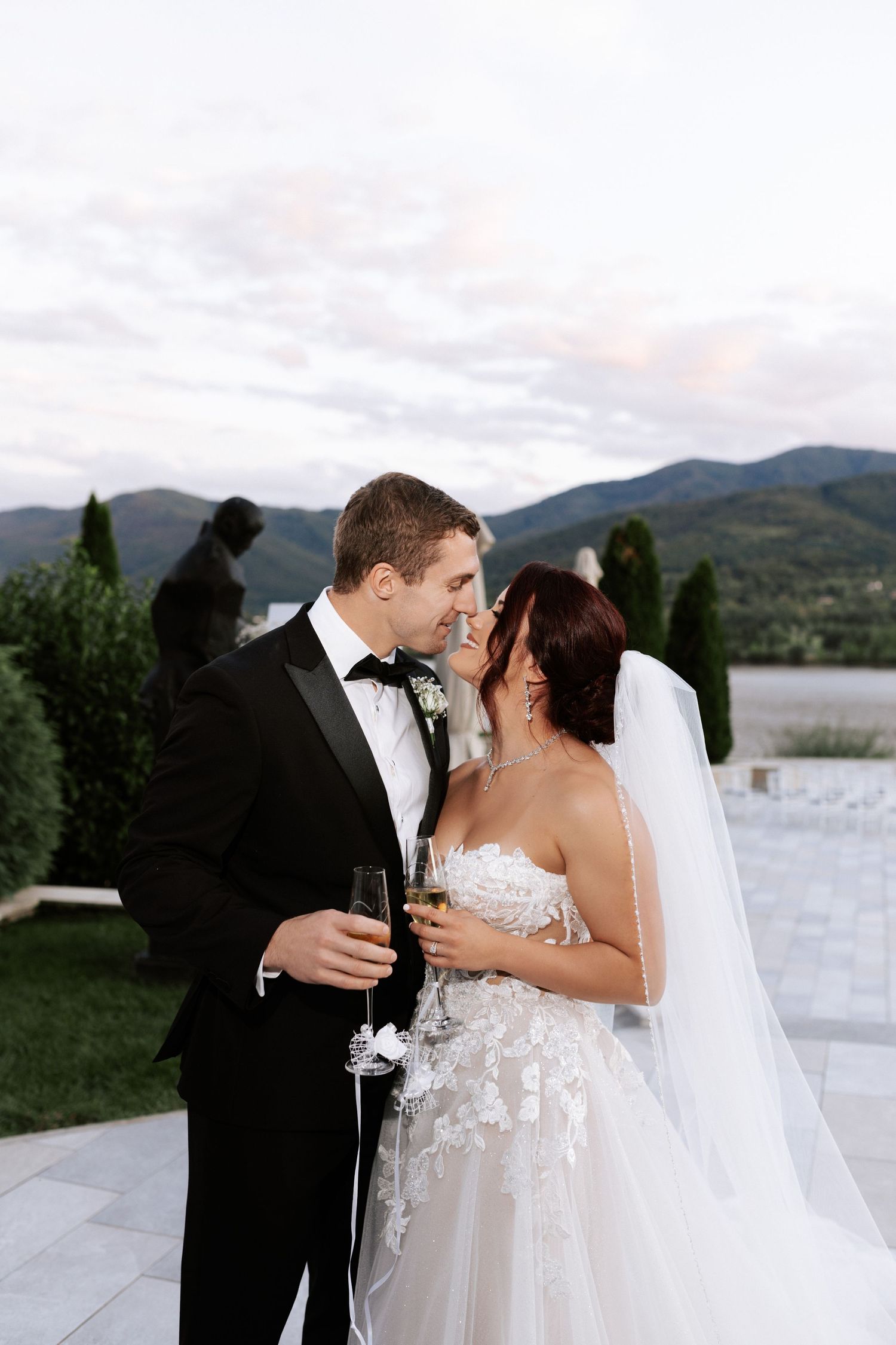 Romantic wedding couple sharing champagne outdoors with mountain views.