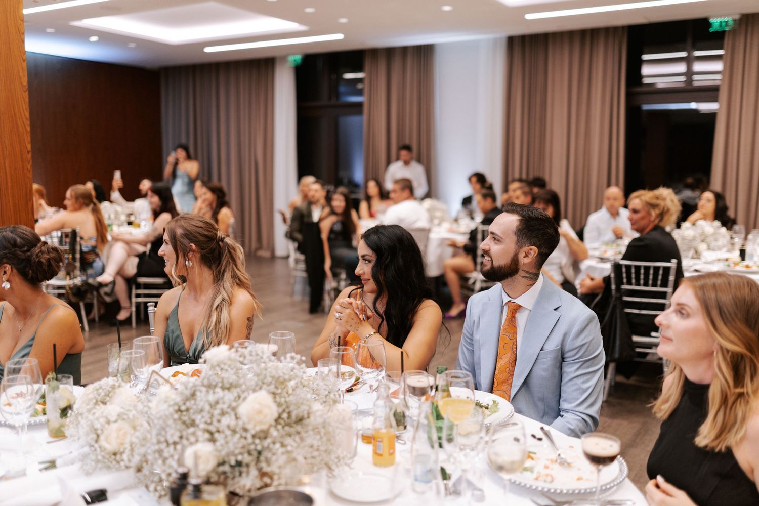 Wedding reception guests seated at round tables with elegant white floral centerpieces.