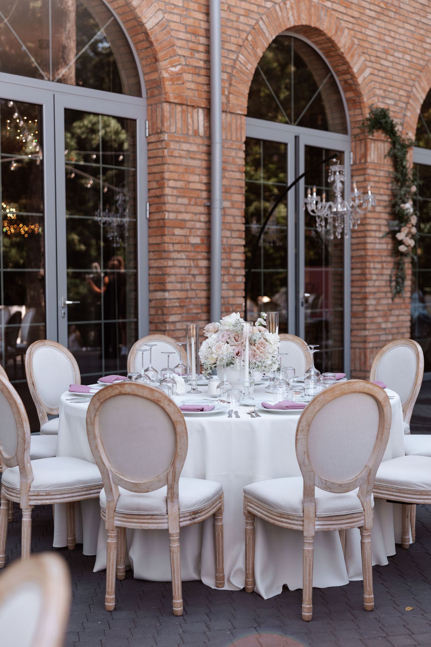 Elegant wedding reception venue with arched brick walls, crystal chandeliers, and white upholstered dining chairs.