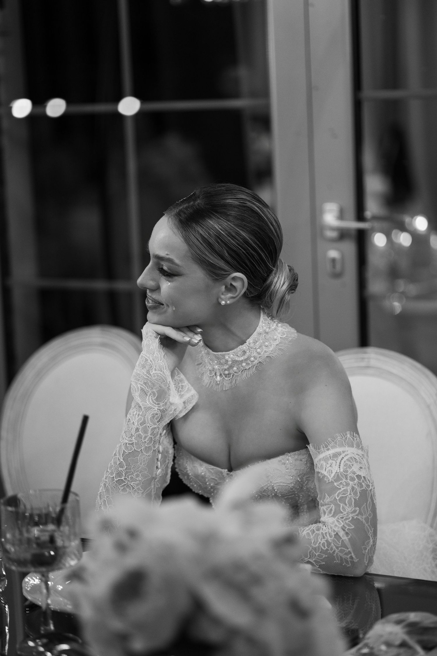 A bride in lace rests on a white couch during her wedding reception.