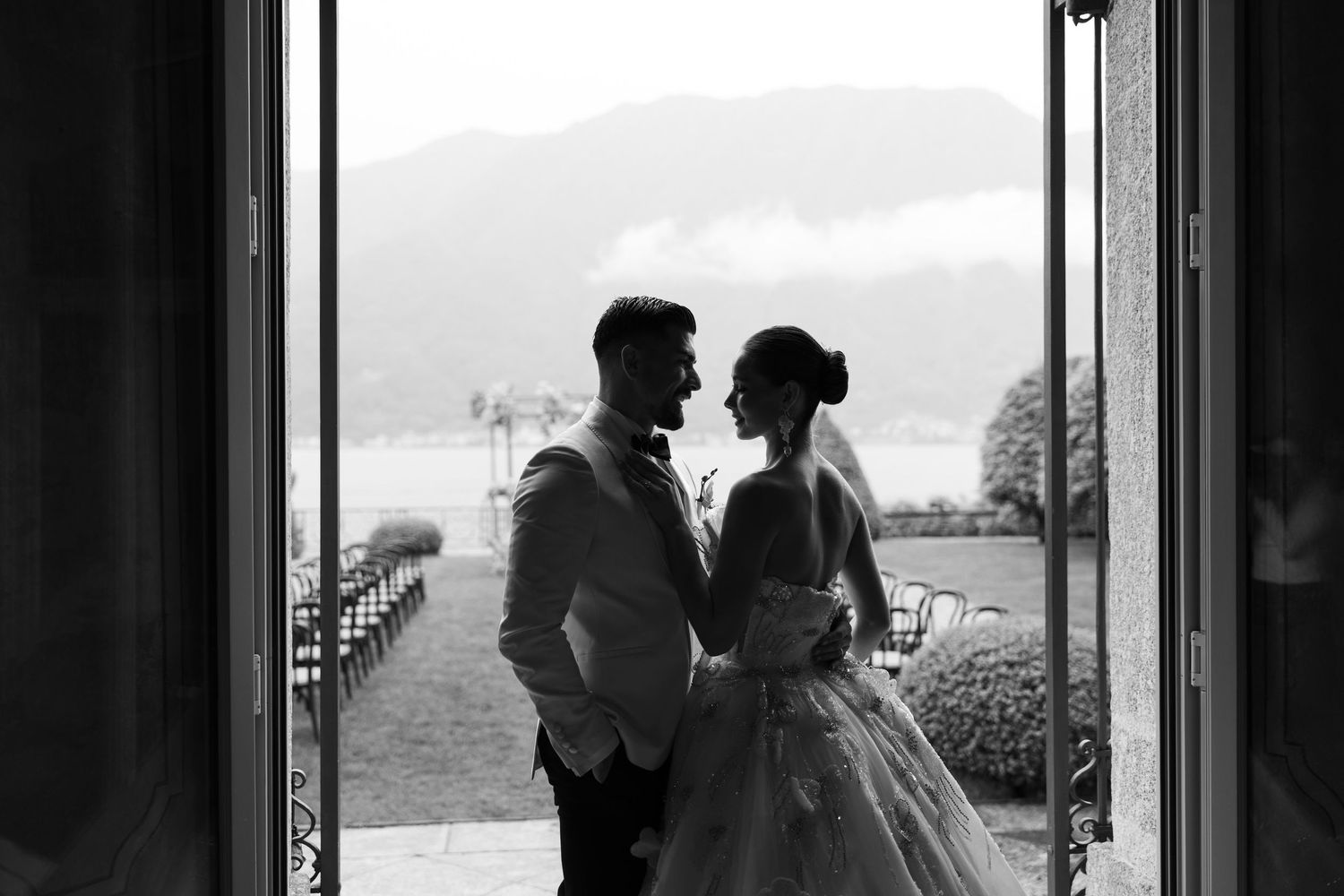 A romantic black and white photo shows a couple embracing by a window in silhouette.