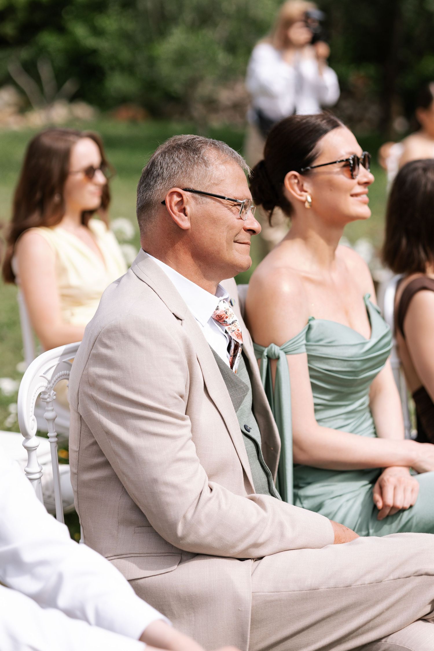 Wedding guests in mint green dresses and beige suits sit outdoors during a summer ceremony.