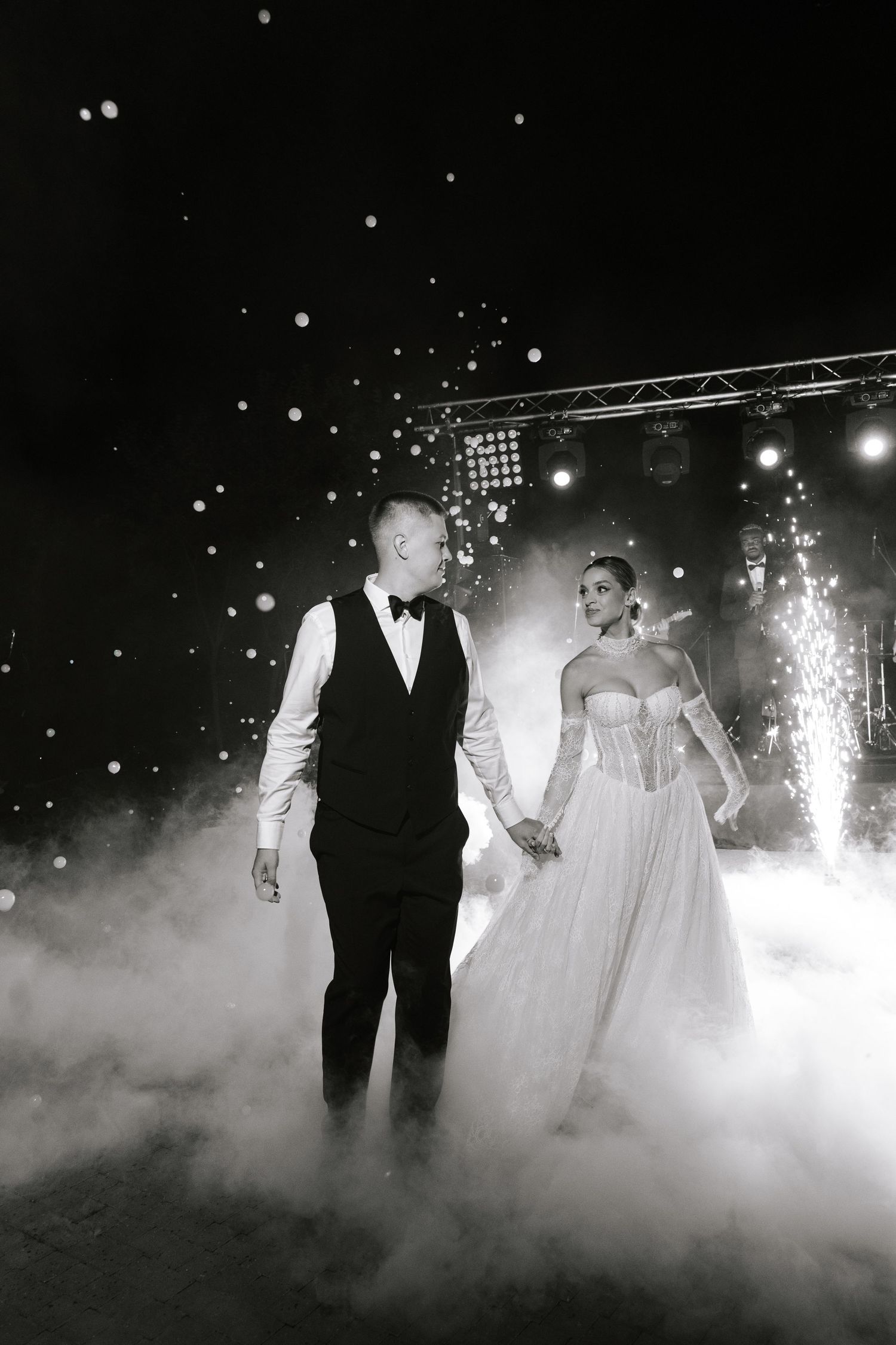 Dramatic black and white photo of couple walking through fog and sparkles on dance floor.
