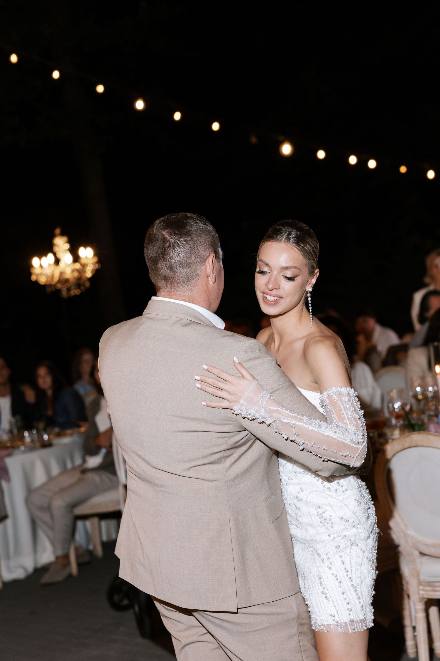 A couple shares a romantic dance moment under string lights at their wedding reception.