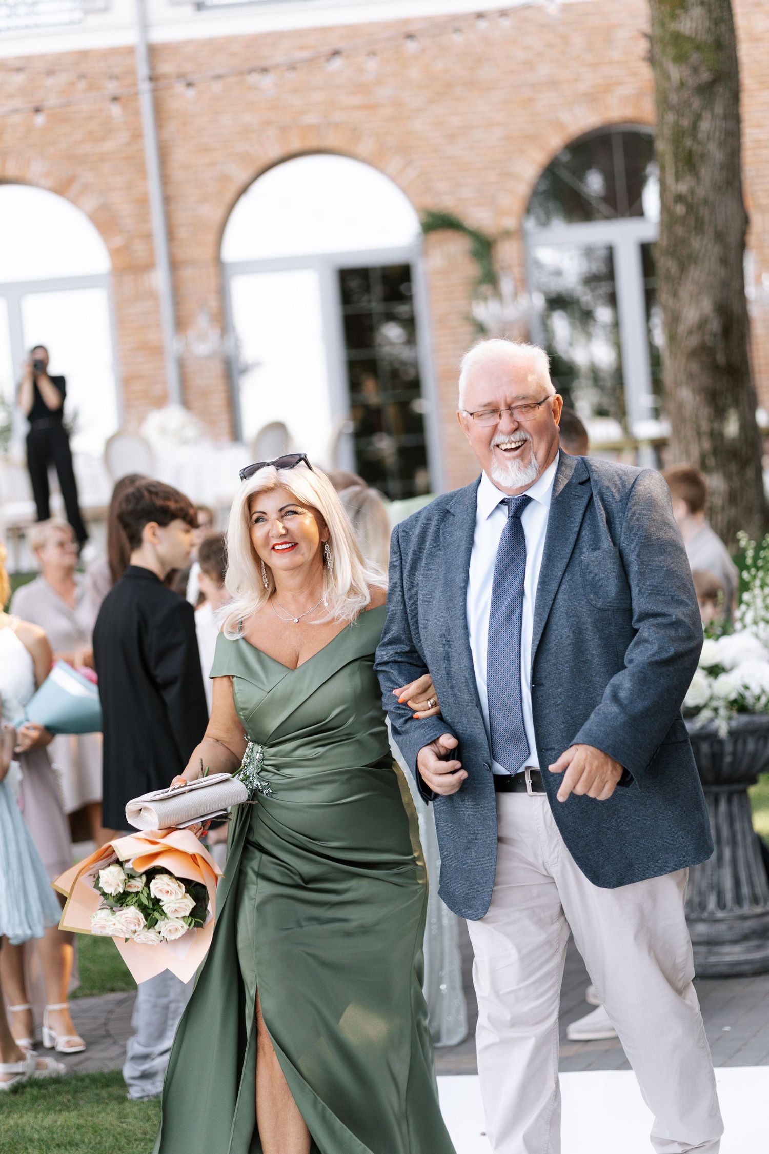 Wedding guests in formal attire share joyful laughter during an outdoor celebration.