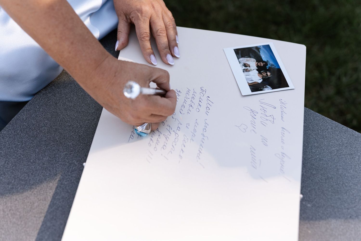 Close-up of hands writing in a wedding guest book with a photo attached.