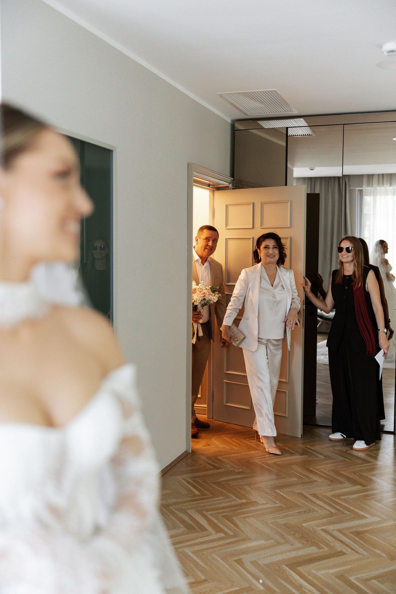 A bright hotel hallway with herringbone flooring and people preparing for a wedding ceremony.