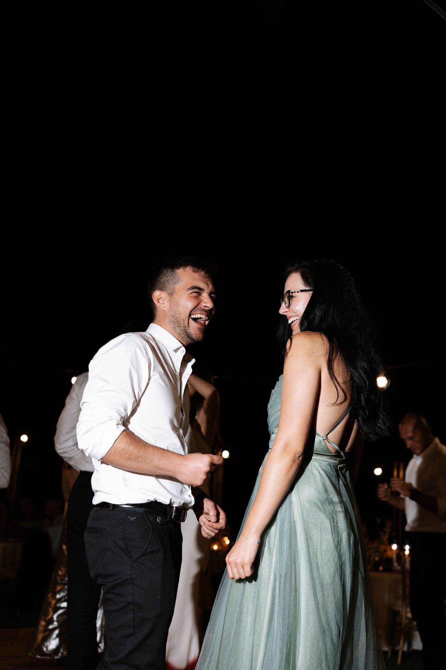 A couple shares a joyful moment dancing together at a nighttime event, with the woman wearing a mint green dress.
