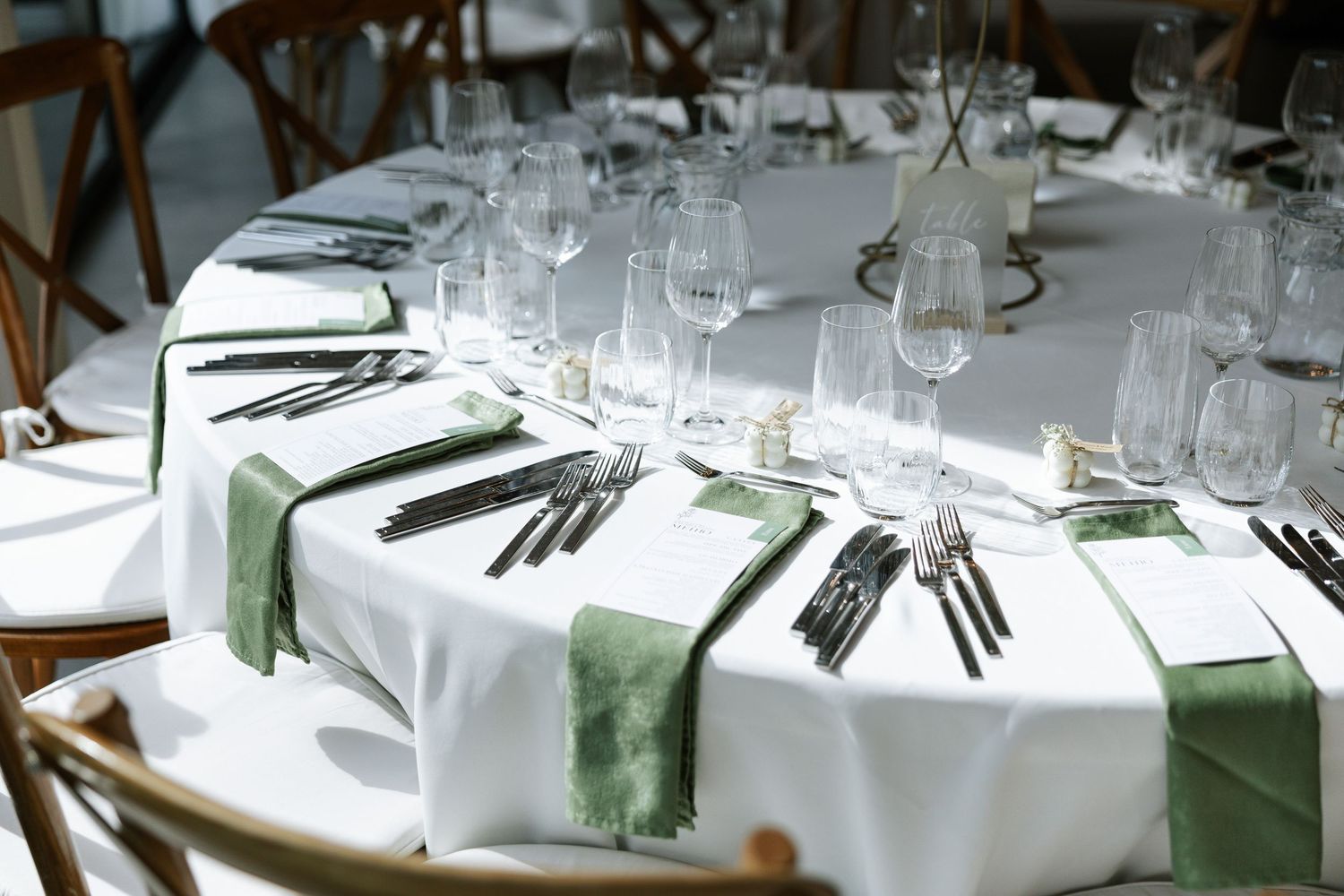 Elegant wedding reception tables set with white linens, green napkins, and crystal glassware in a formal dining arrangement.