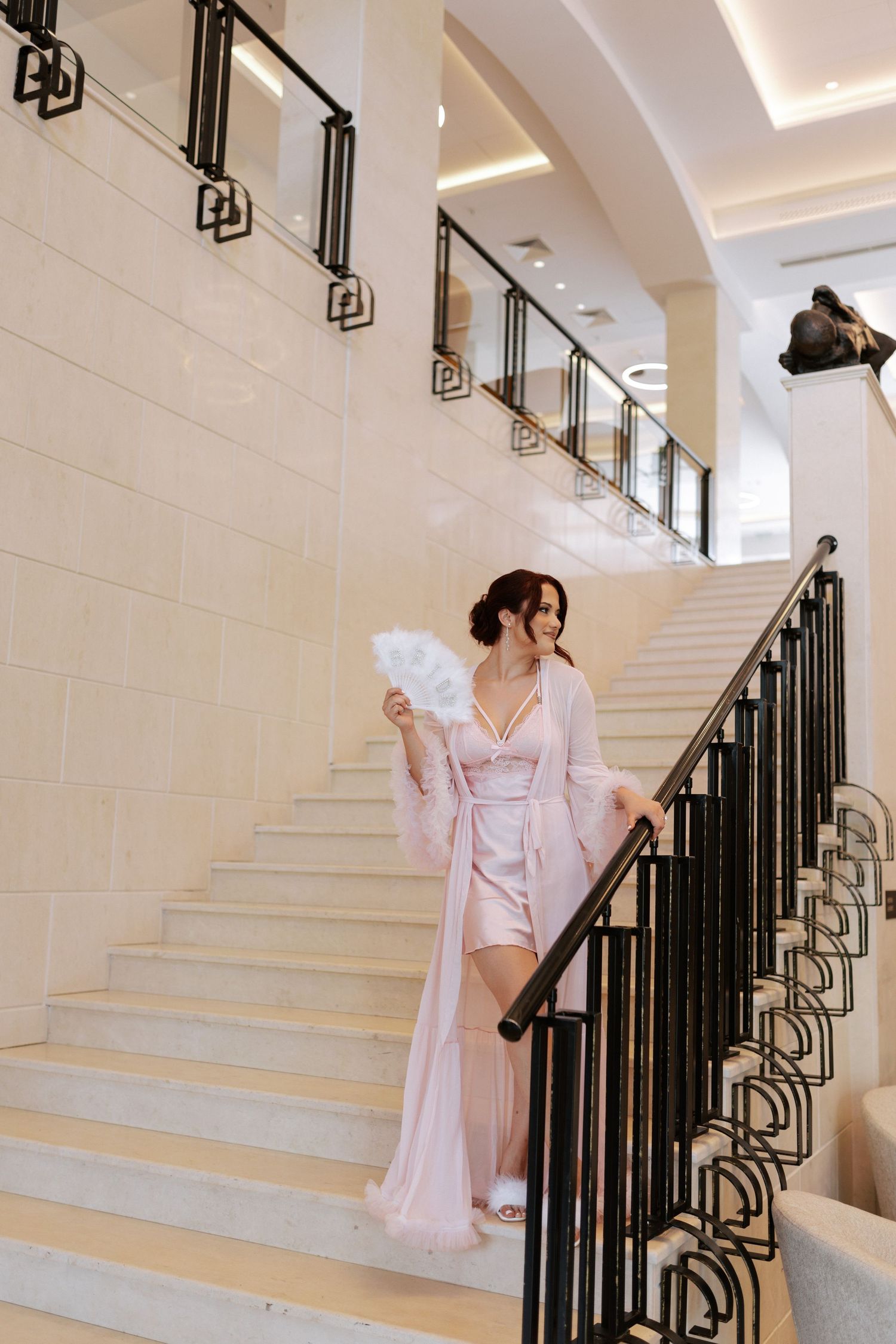 Person in pink robe descending elegant white staircase with ornate black railing.