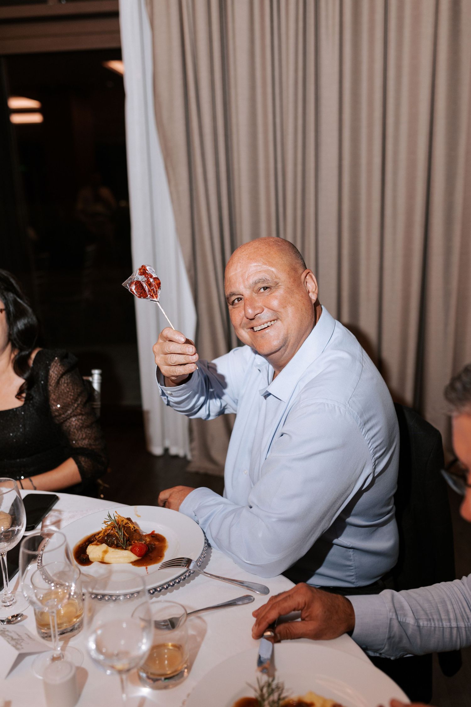 Wedding guest enjoys dinner while gesturing at elegant reception table.