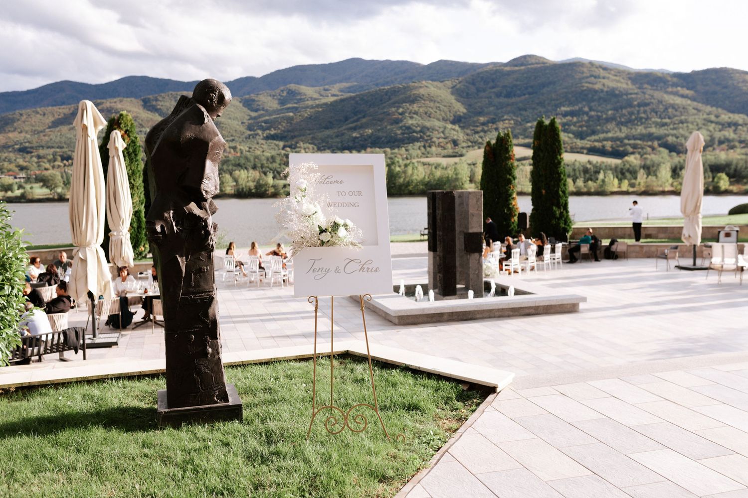 Outdoor wedding venue with mountain views featuring white chairs and cypress trees on a stone patio.