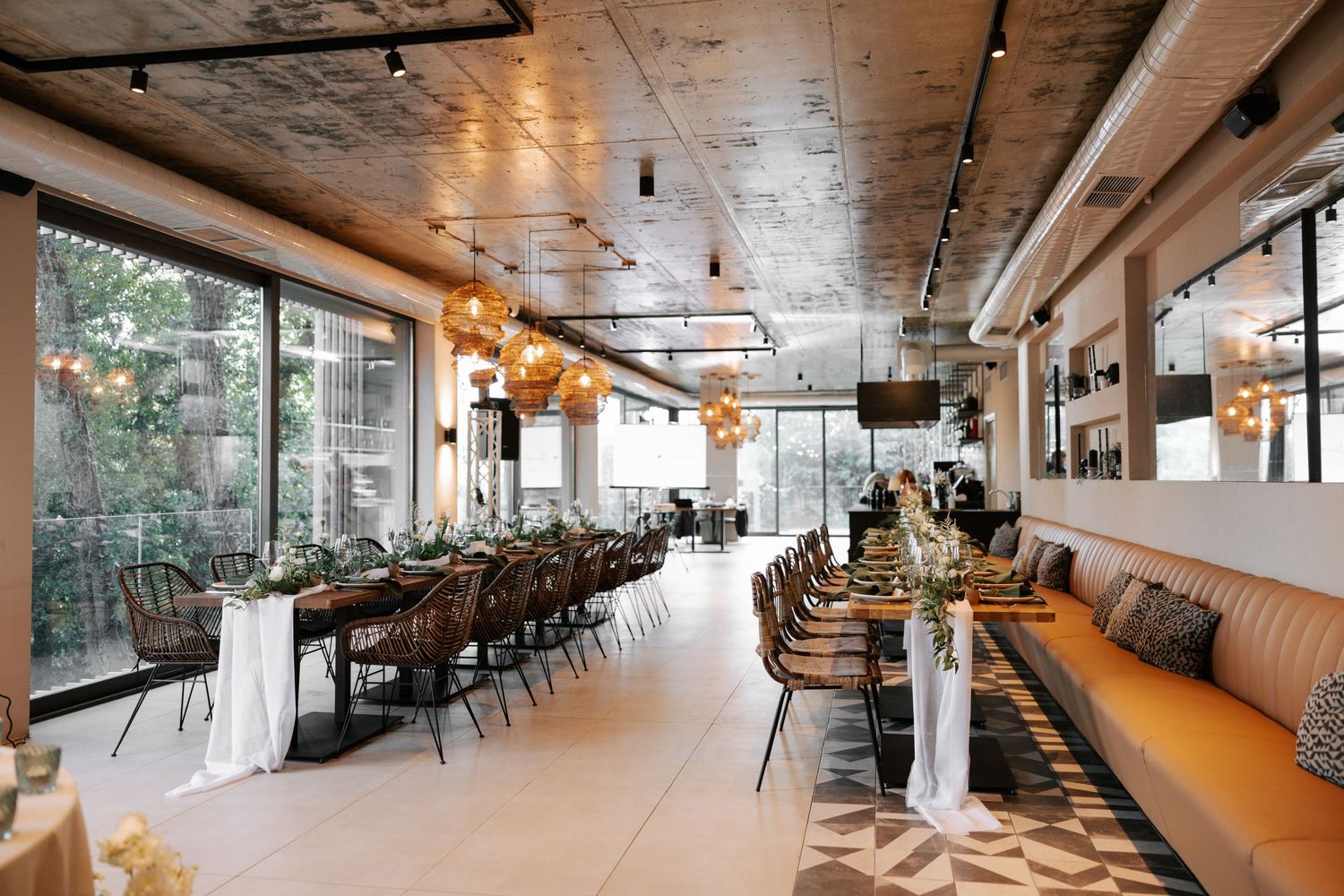 Modern restaurant interior with orange banquette seating, dark chairs and large windows letting in natural light.
