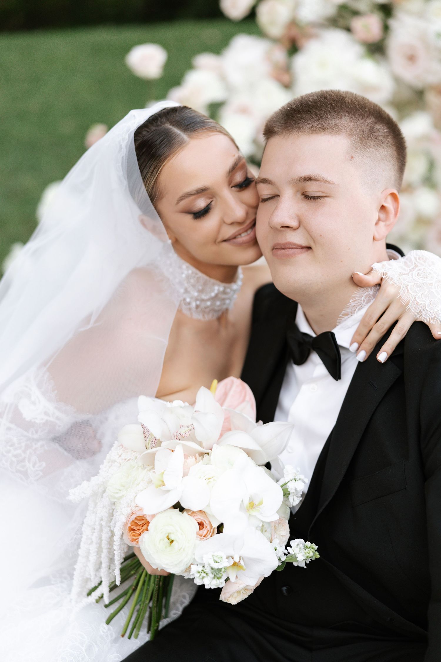 Newlyweds share an intimate moment with white flowers against a garden backdrop.