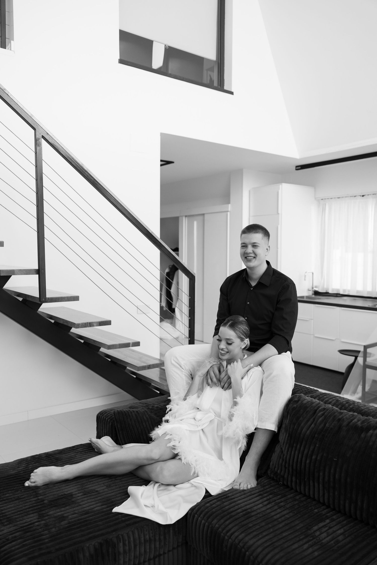 Couple relaxing on dark couch in modern home interior with staircase.