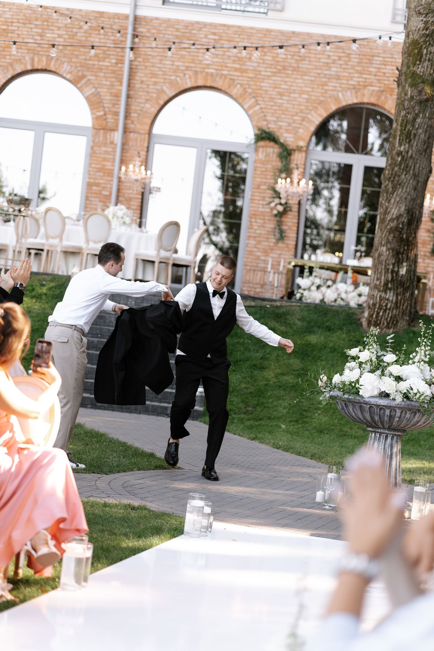 Wedding guests dancing and celebrating at outdoor reception with brick building backdrop.