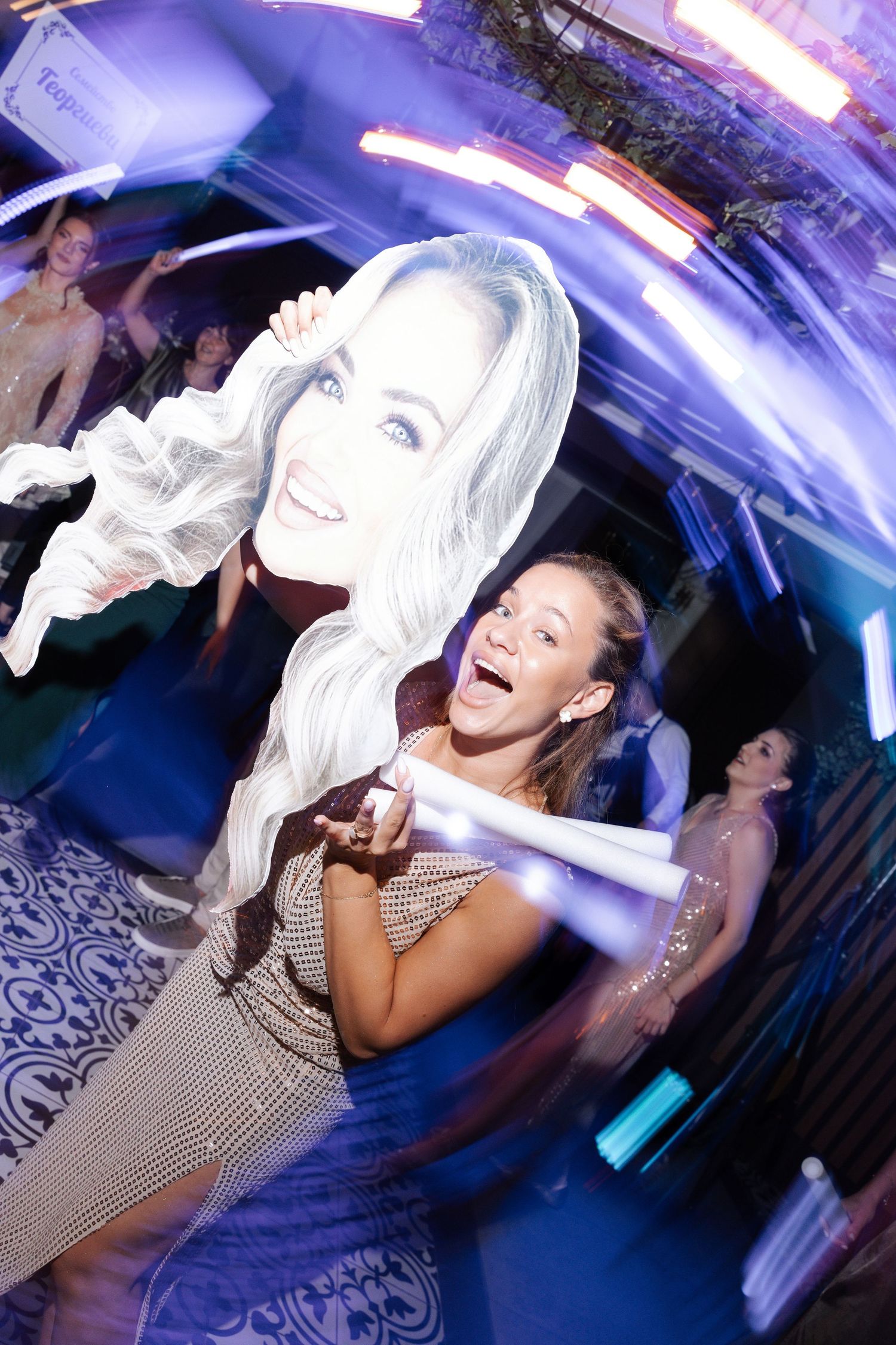 A woman in a checkered dress dances energetically at a nightclub under blue and purple lighting.