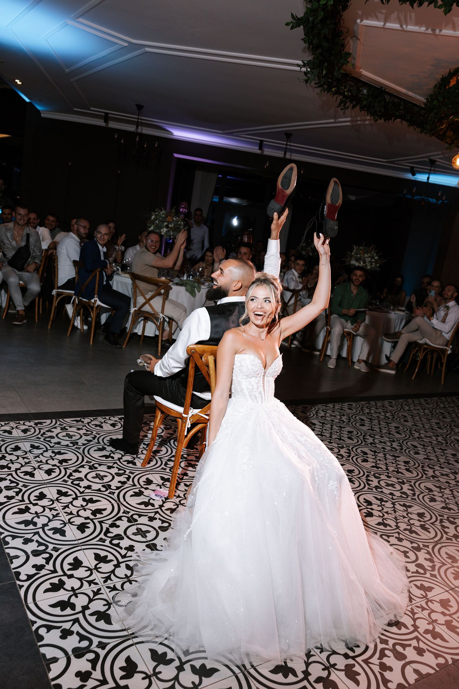 A bride in a flowing white gown dances joyfully on a patterned dance floor at a wedding reception.