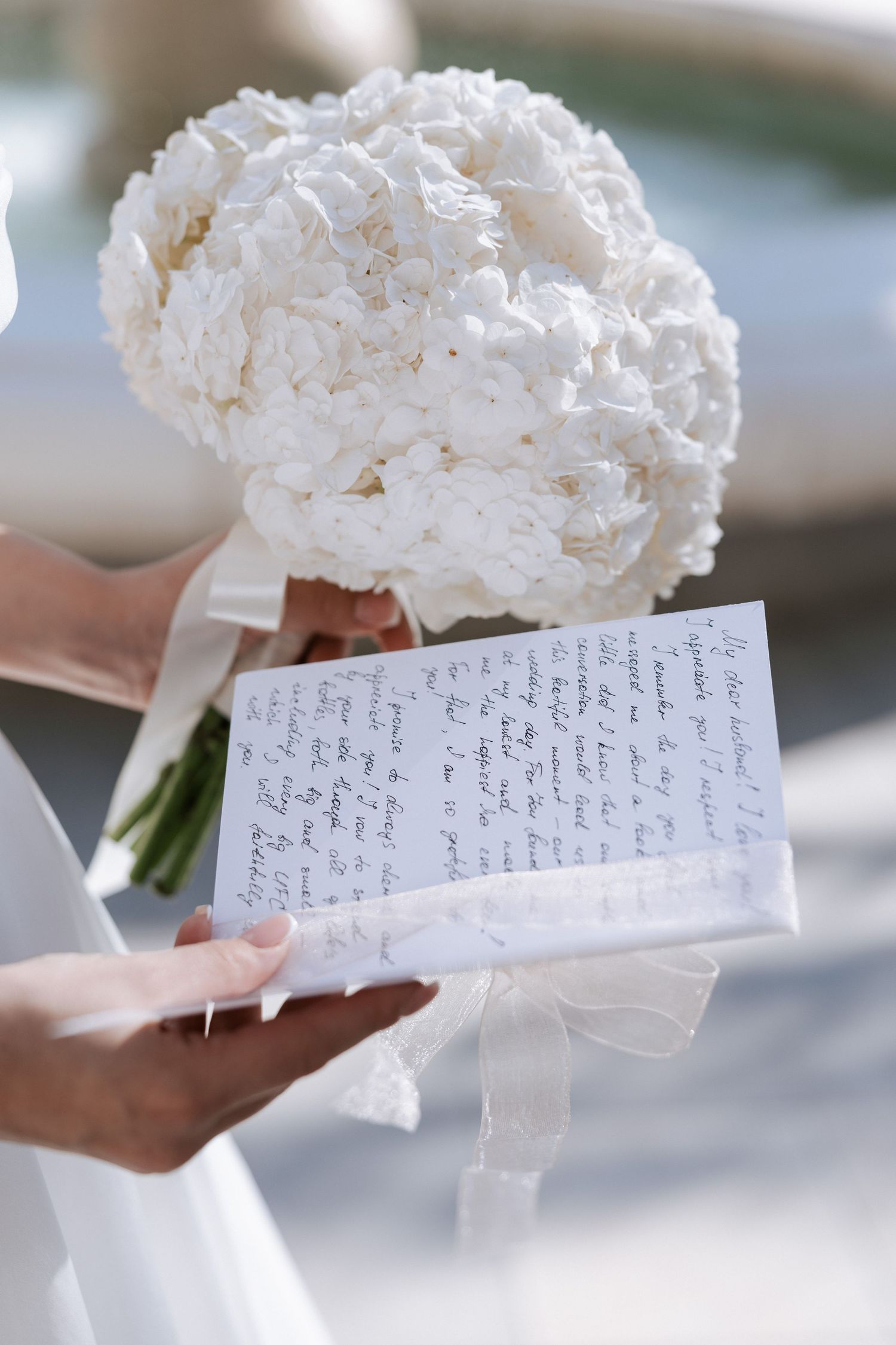 A handwritten wedding vow note held next to a white hydrangea bouquet.