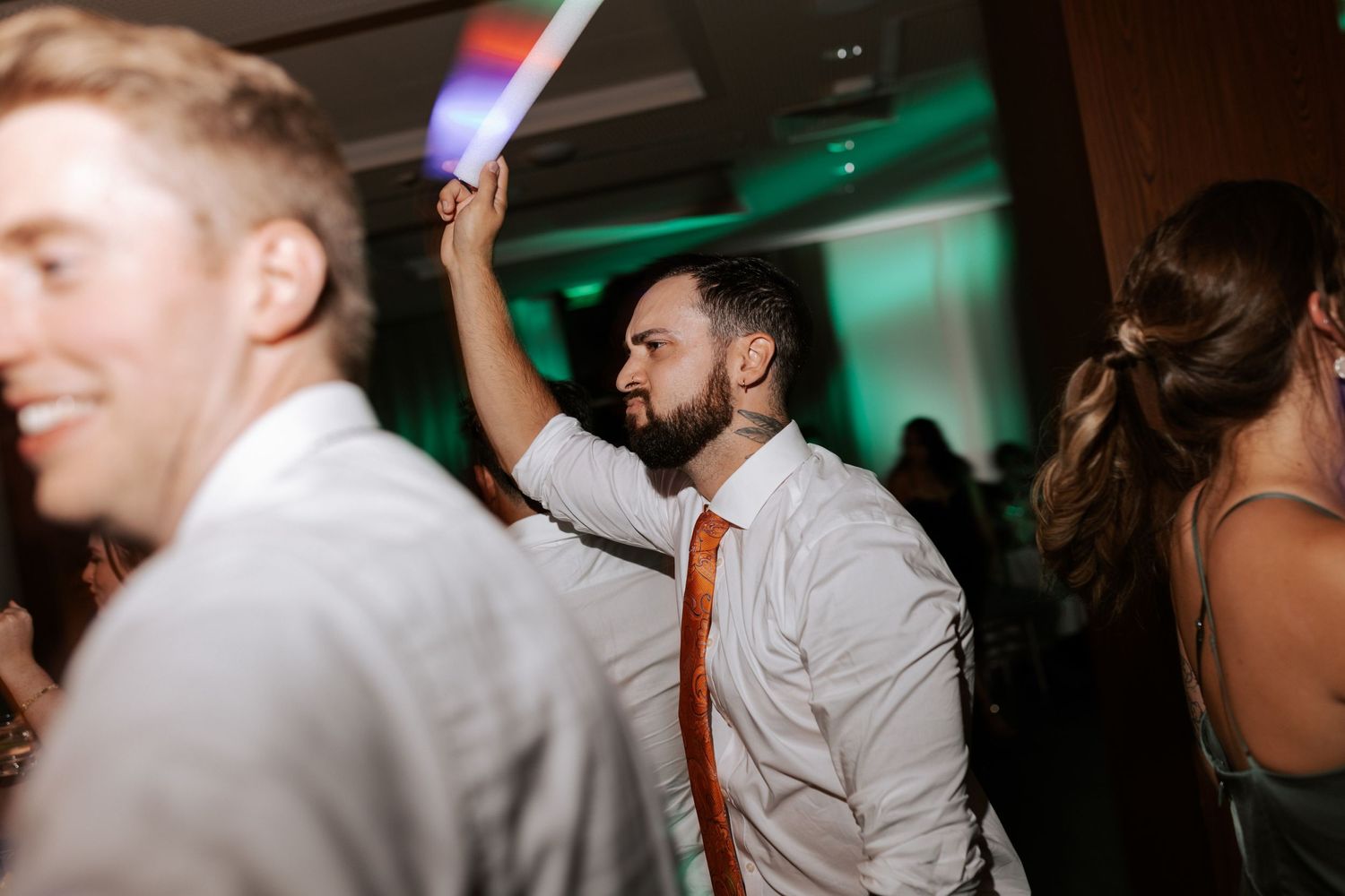 Party guests dance with light-up LED sticks in a dimly lit reception venue.