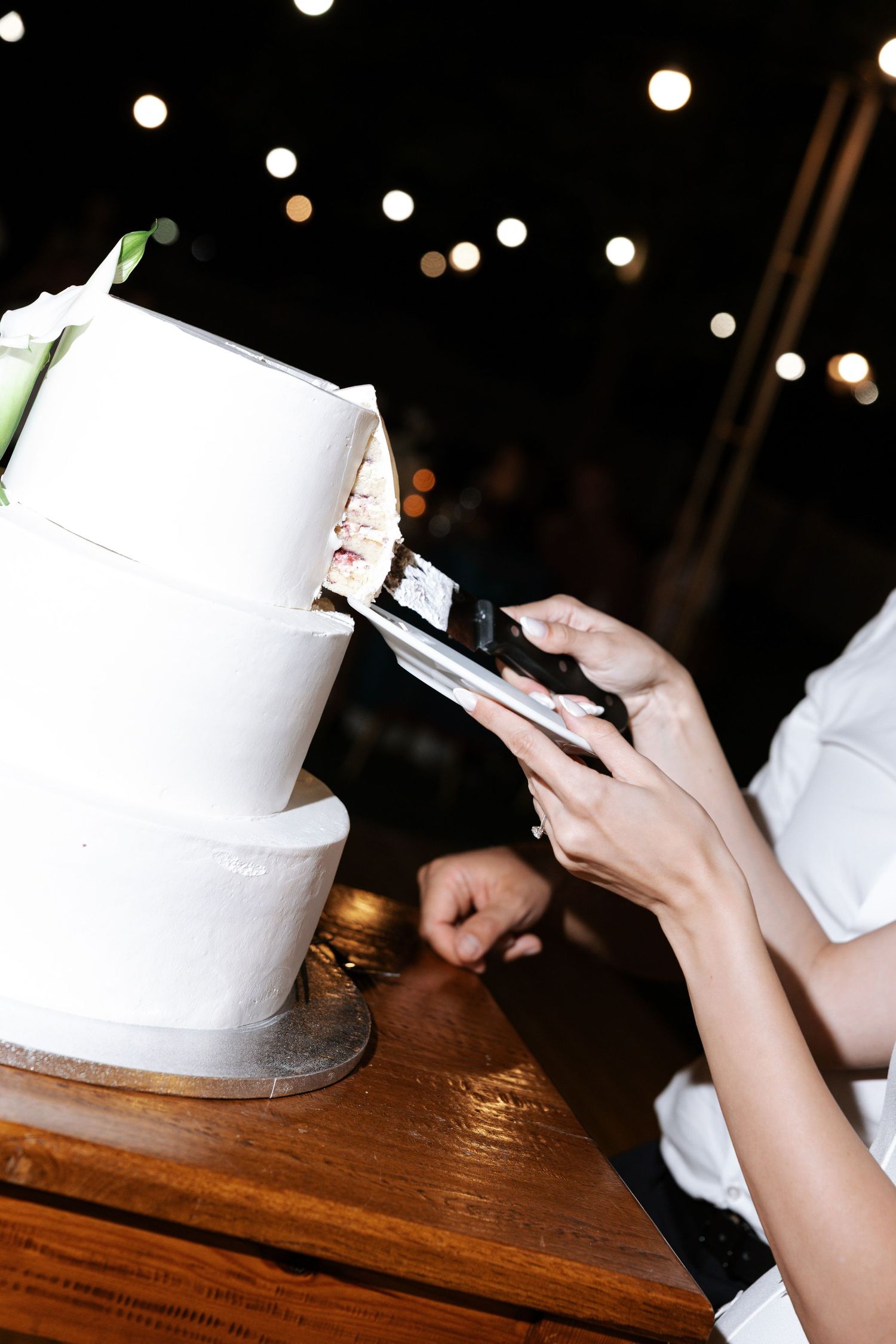 Person using smartphone while sitting at wooden table with white ceramic teapot in dim lighting.