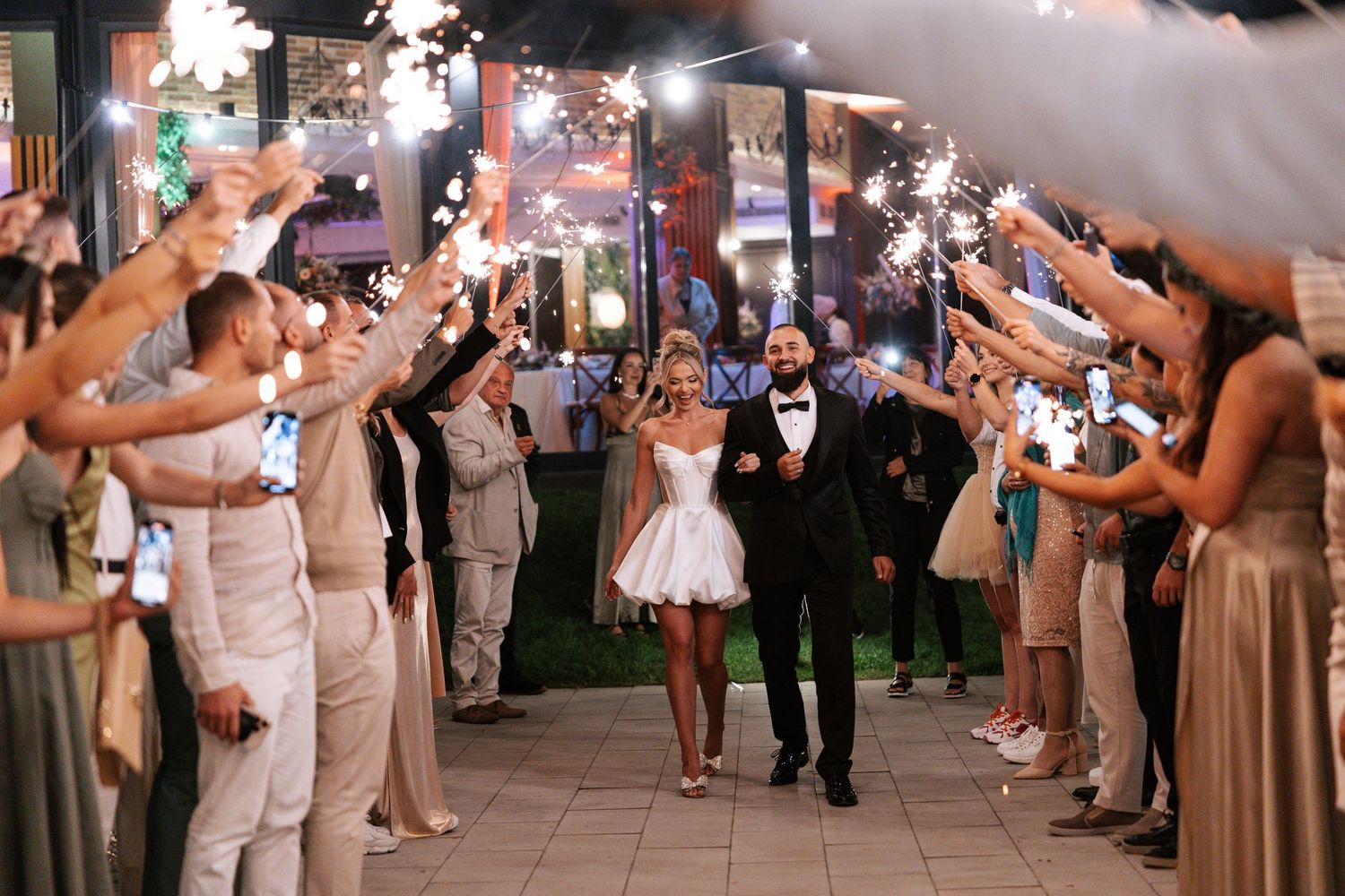 Wedding guests hold sparklers creating a magical illuminated walkway for the newlywed couple at their evening reception exit.