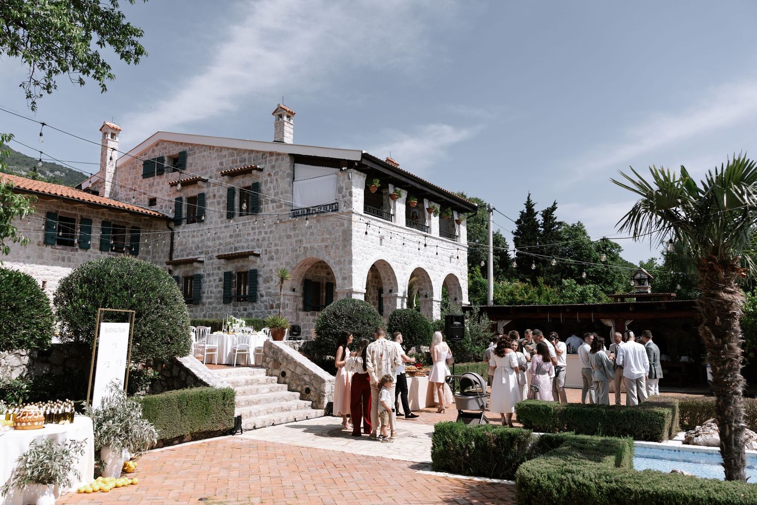 Panoramic view of a Mediterranean villa with white walls, stone architecture, and lush tropical gardens.