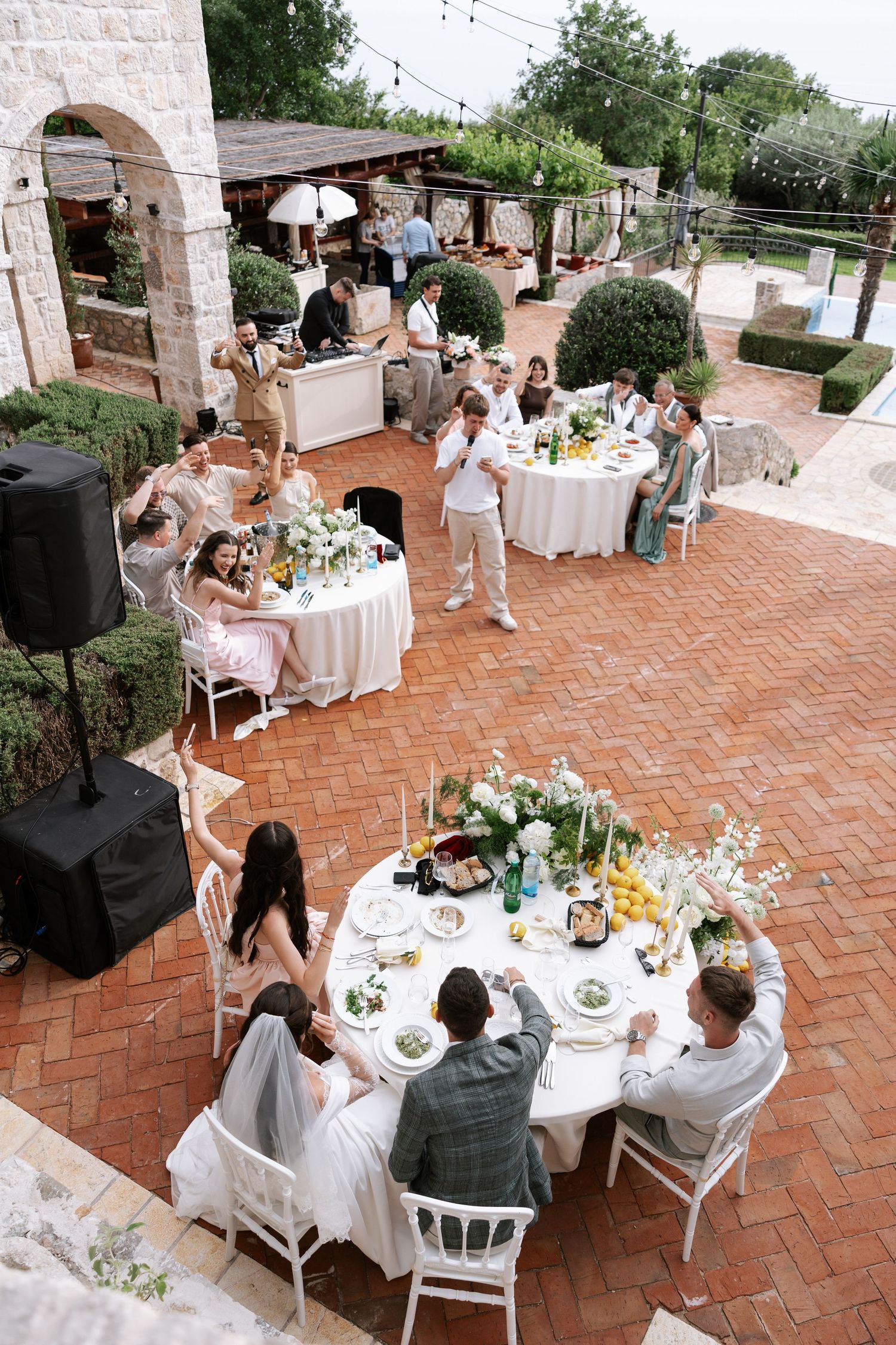 Outdoor wedding reception on terrace with round tables, white linens, and stone archways in Mediterranean setting.