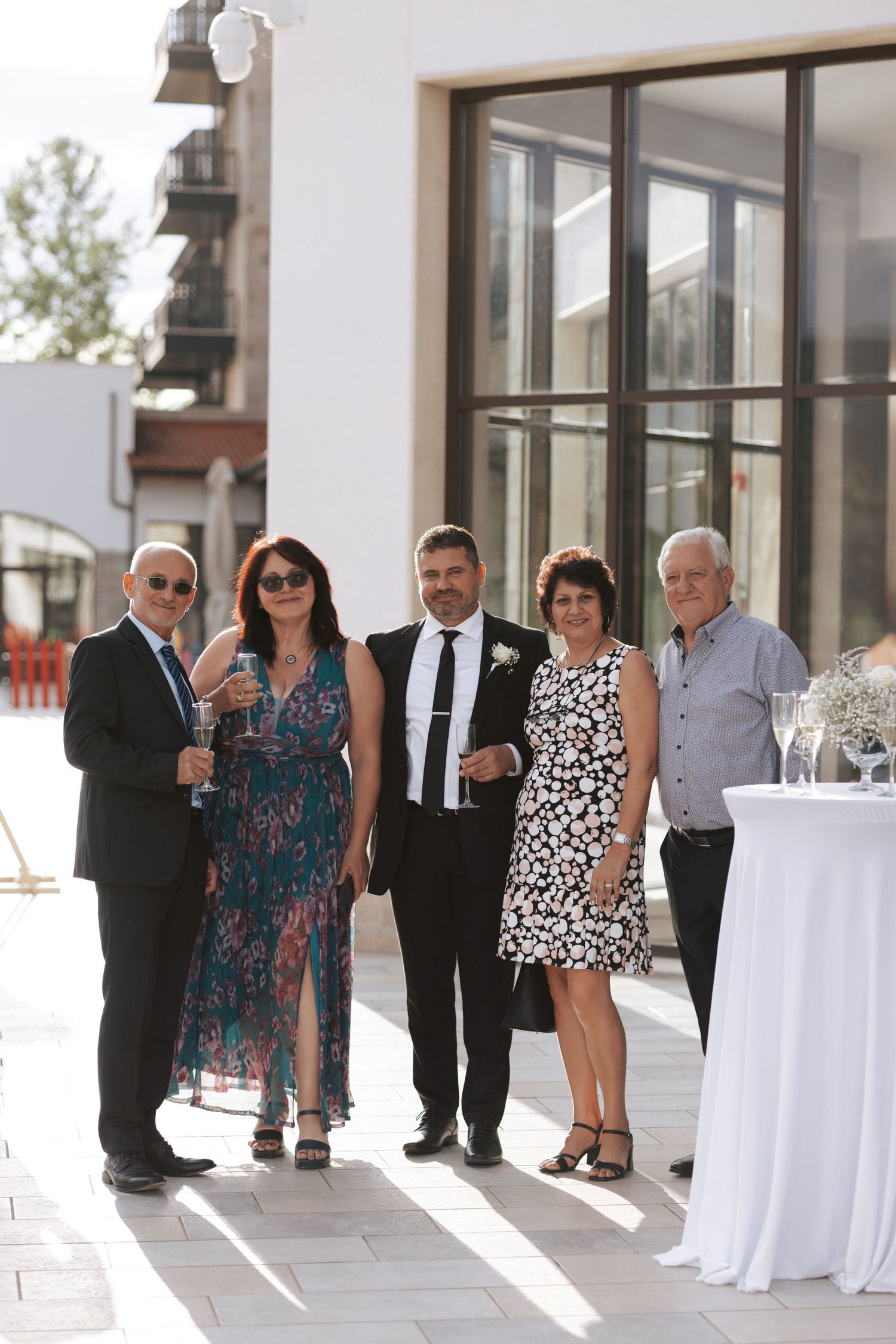 Small group of wedding guests posing by a modern building during daytime celebration.
