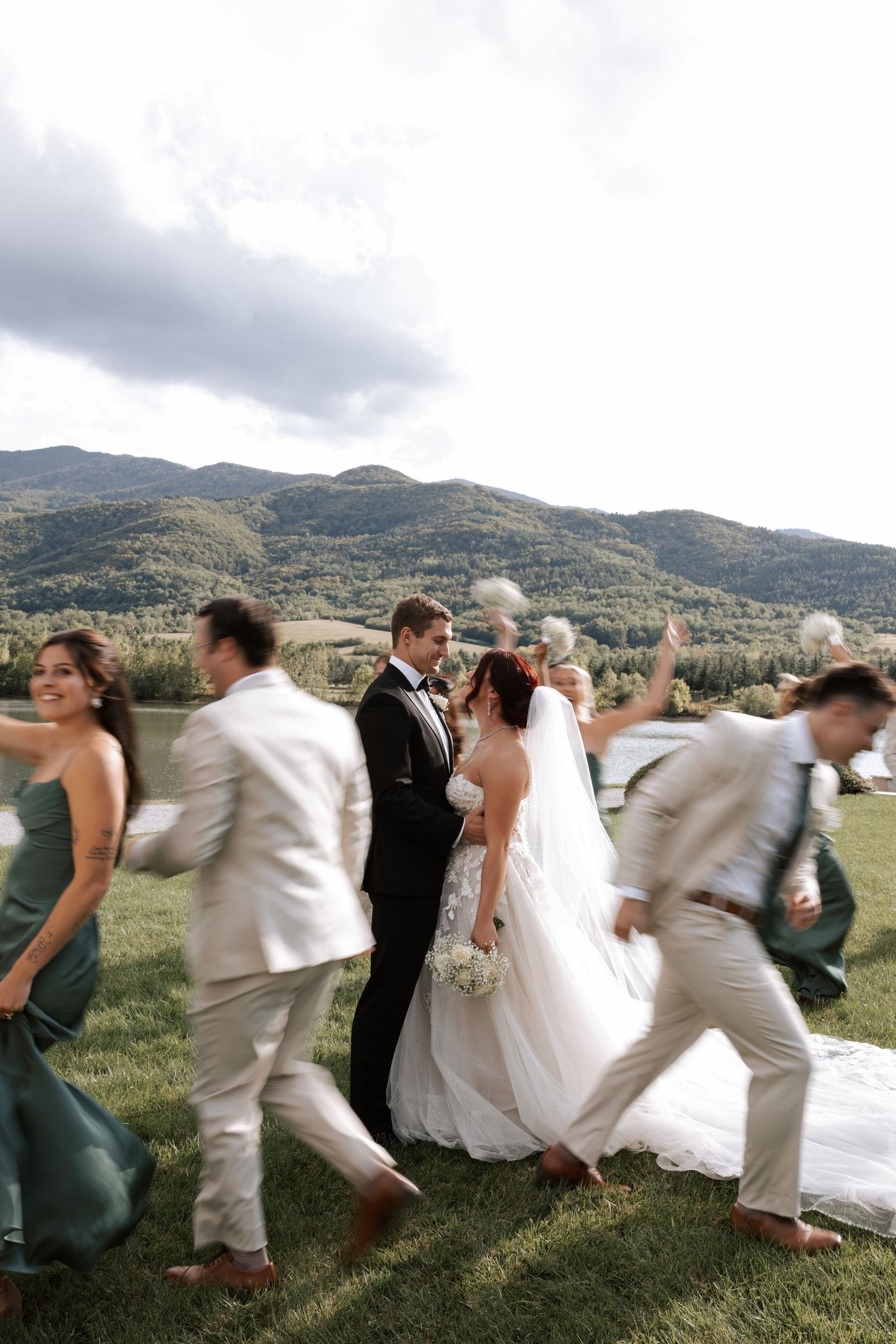 Wedding party runs joyfully across a grassy hilltop with mountains in the background.
