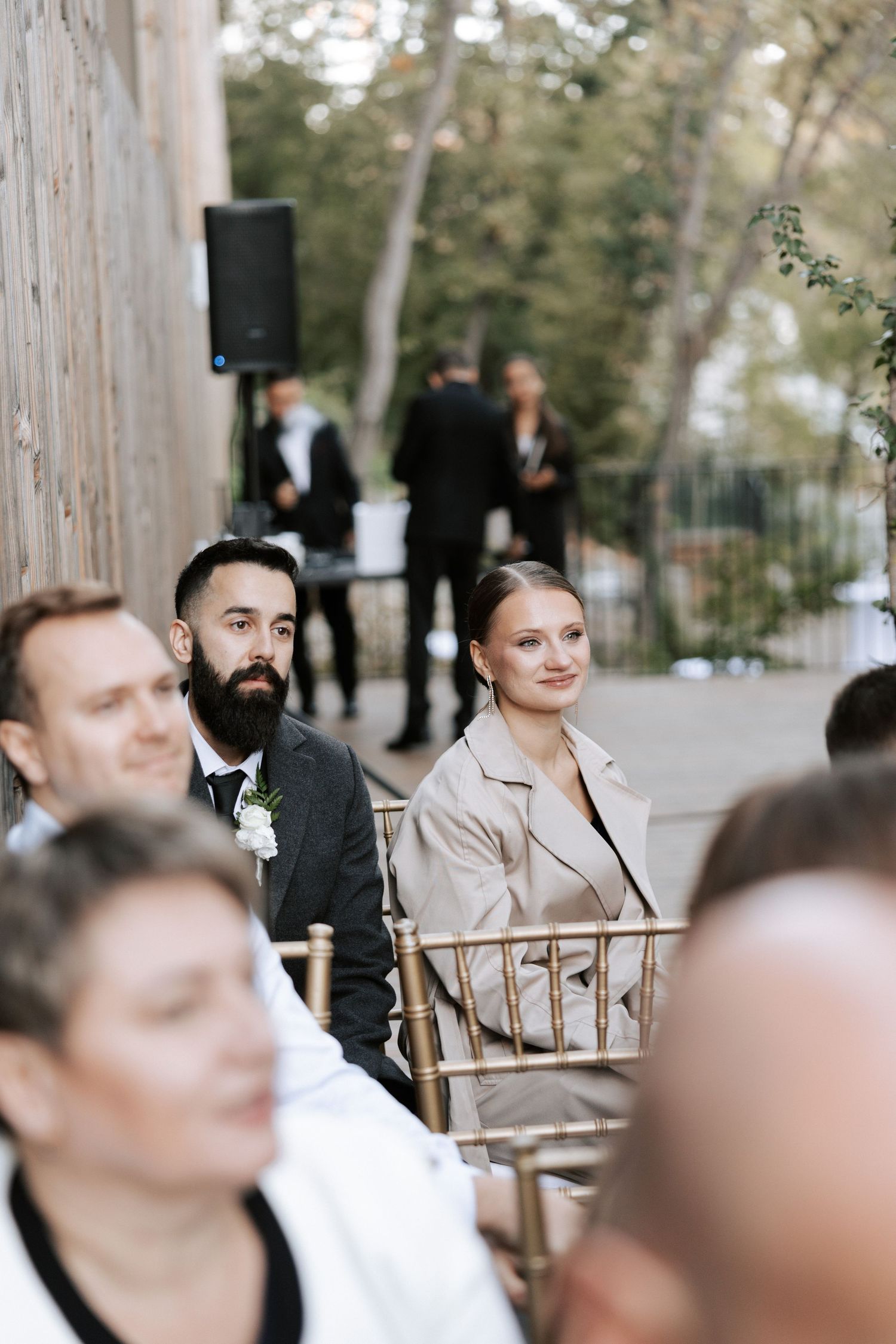 Wedding guests seated at an outdoor ceremony with natural woodland backdrop.