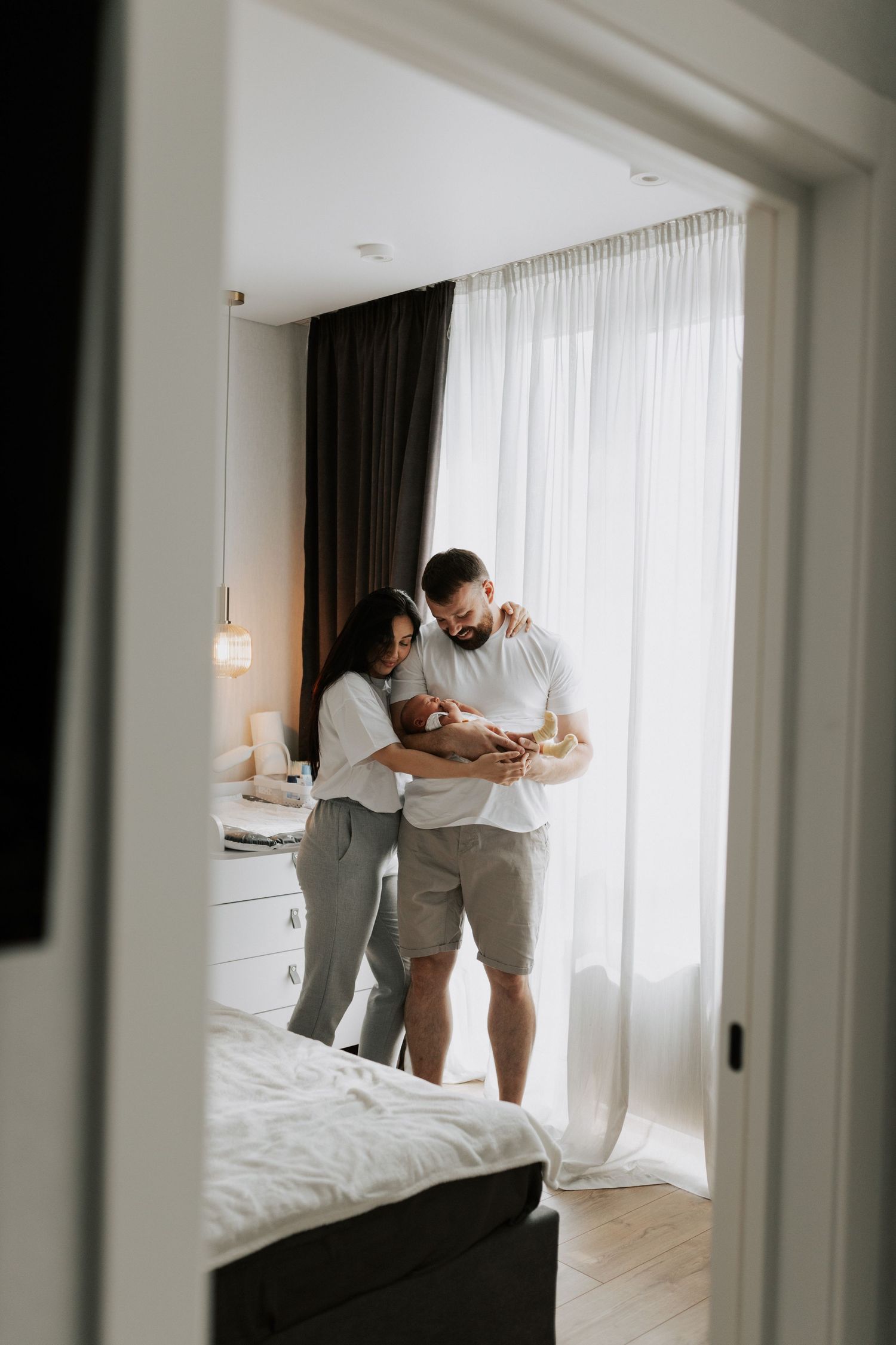 A candid family scene through a doorway showing parents holding their newborn.