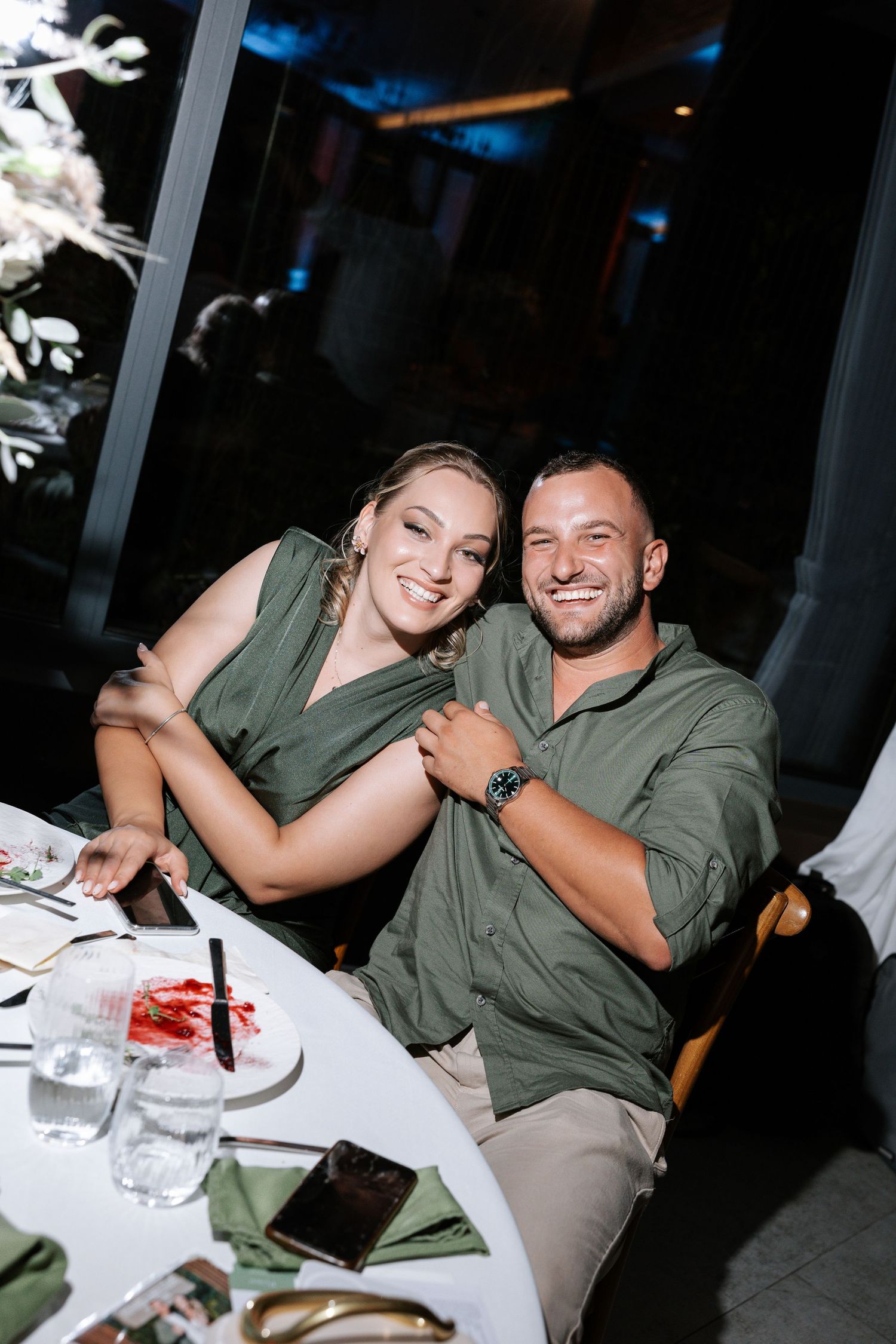Candid sequence of a couple laughing together at a casual dinner table wearing matching olive green shirts.